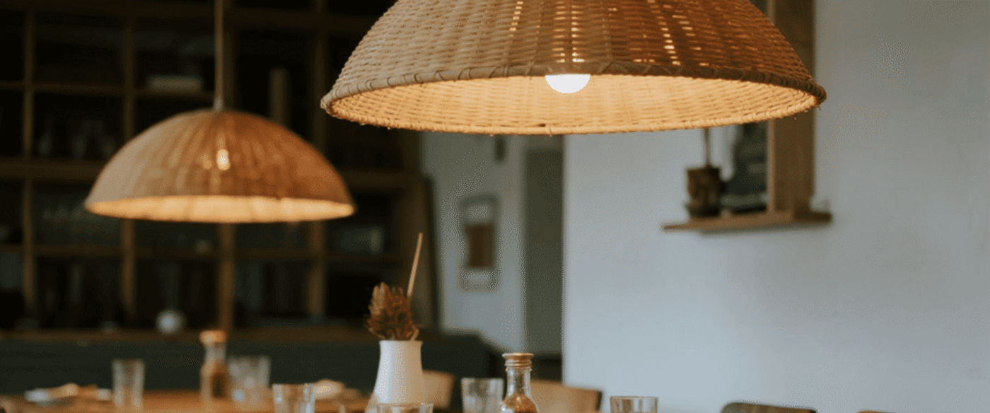 Cozy dining table set with plates, glasses, and napkins under warm, woven pendant lights in a modern, rustic restaurant interior.