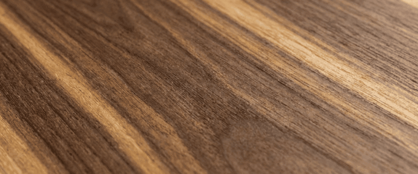 Warm close-up of textured walnut wood grain showing rich brown and tan streaks, natural knots, and a smooth satin finish