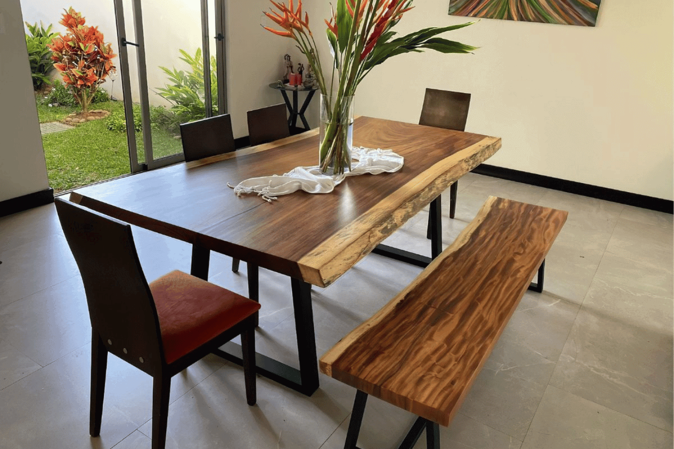 Modern dining set with a live-edge wooden table and bench, complemented by sleek chairs and vibrant floral centerpiece.