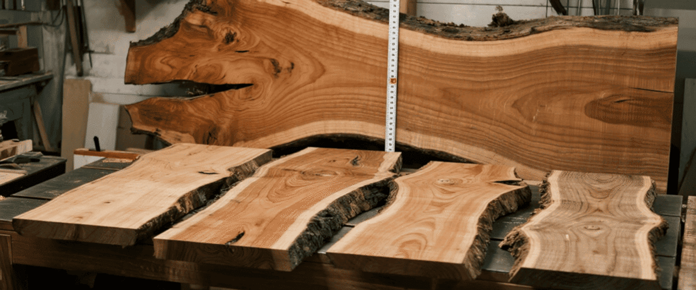 Live-edge walnut slabs on a workshop table showing natural grain, bark edges, and measuring tape for scale.