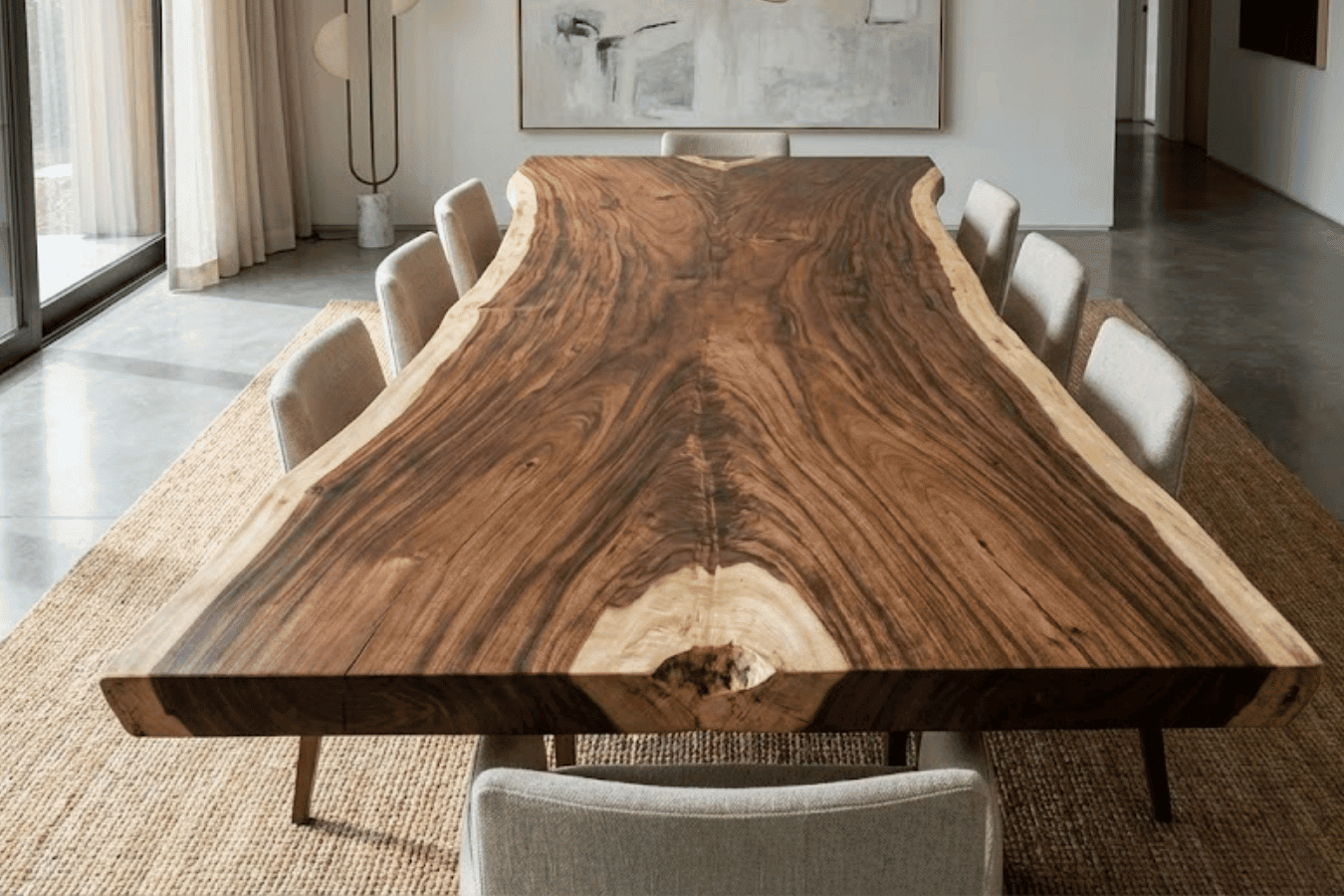 Live-edge walnut dining table with beige upholstered chairs on a woven rug in a bright, modern dining room