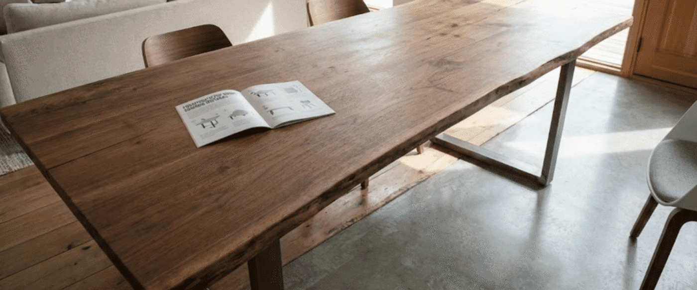 sunlit dining table with a live-edge wooden top, metal legs, chairs, and an open booklet on the surface