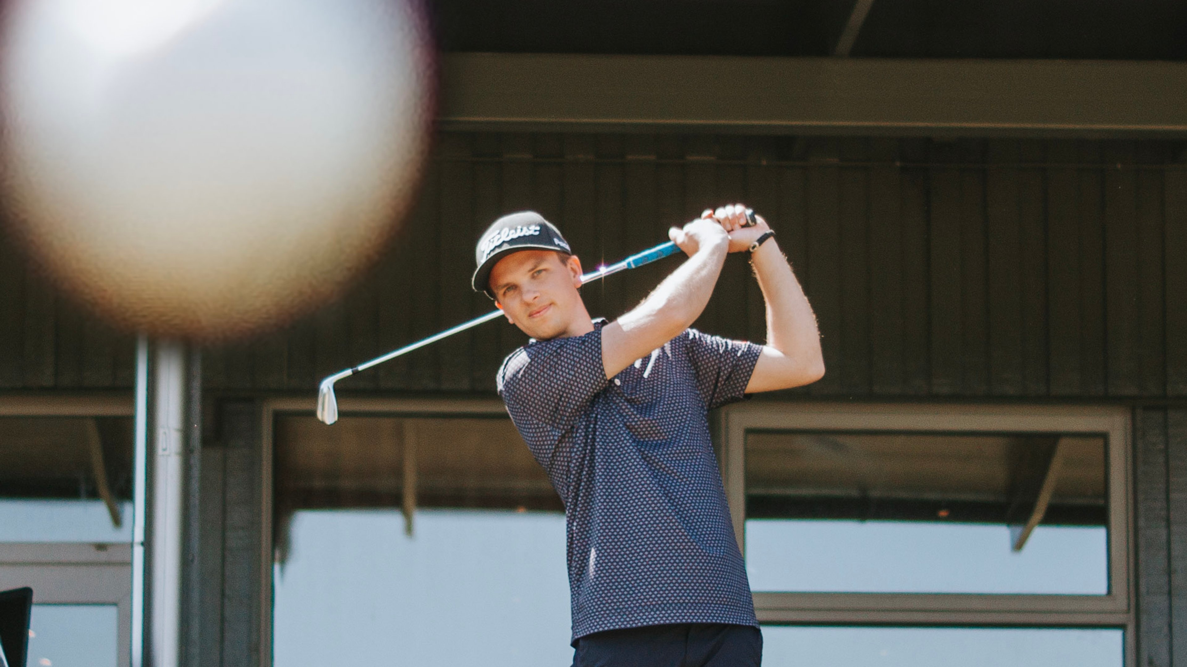 Man på driving range med en boll som flyger mot kameran
