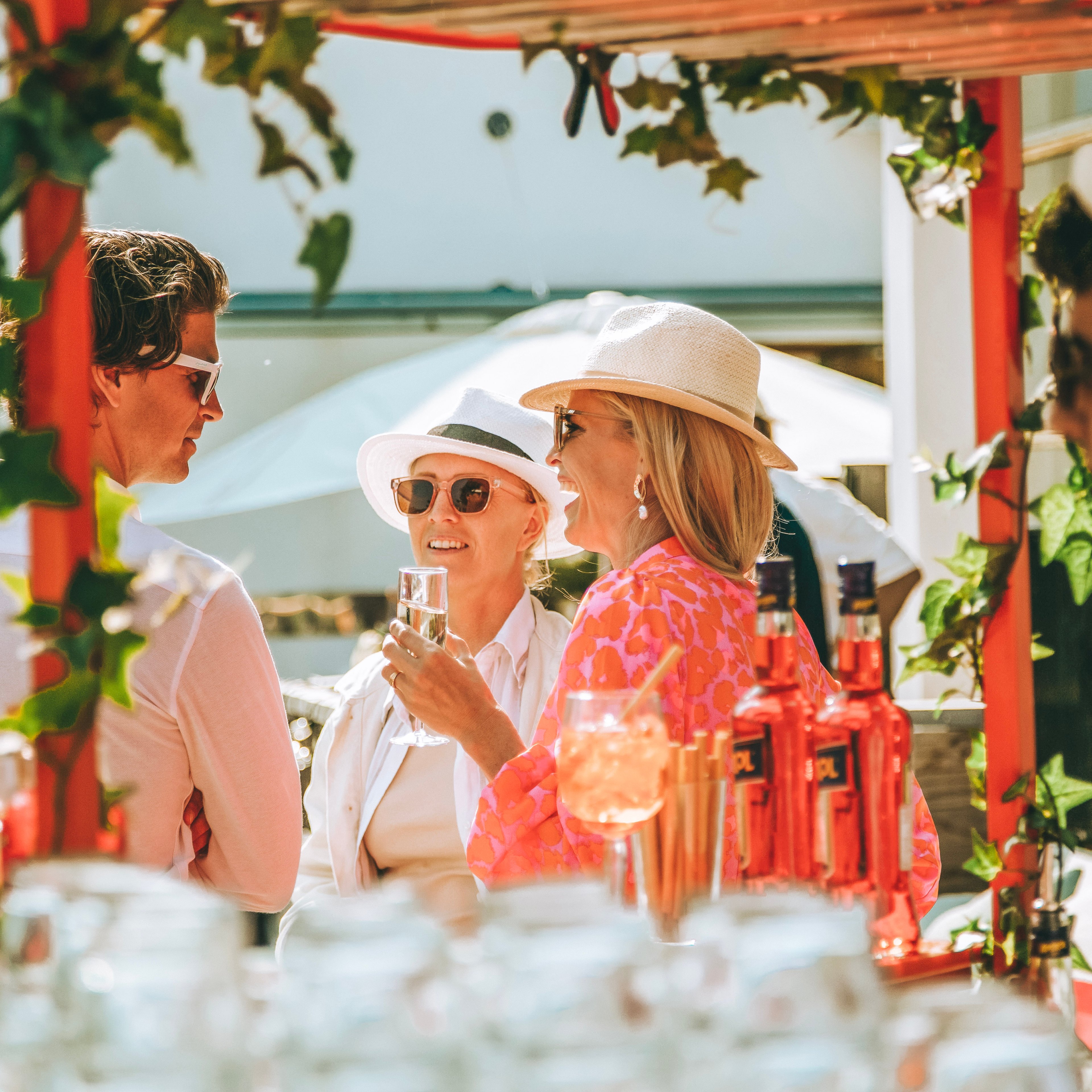 Människor med drinkar i solskenet under en pergola