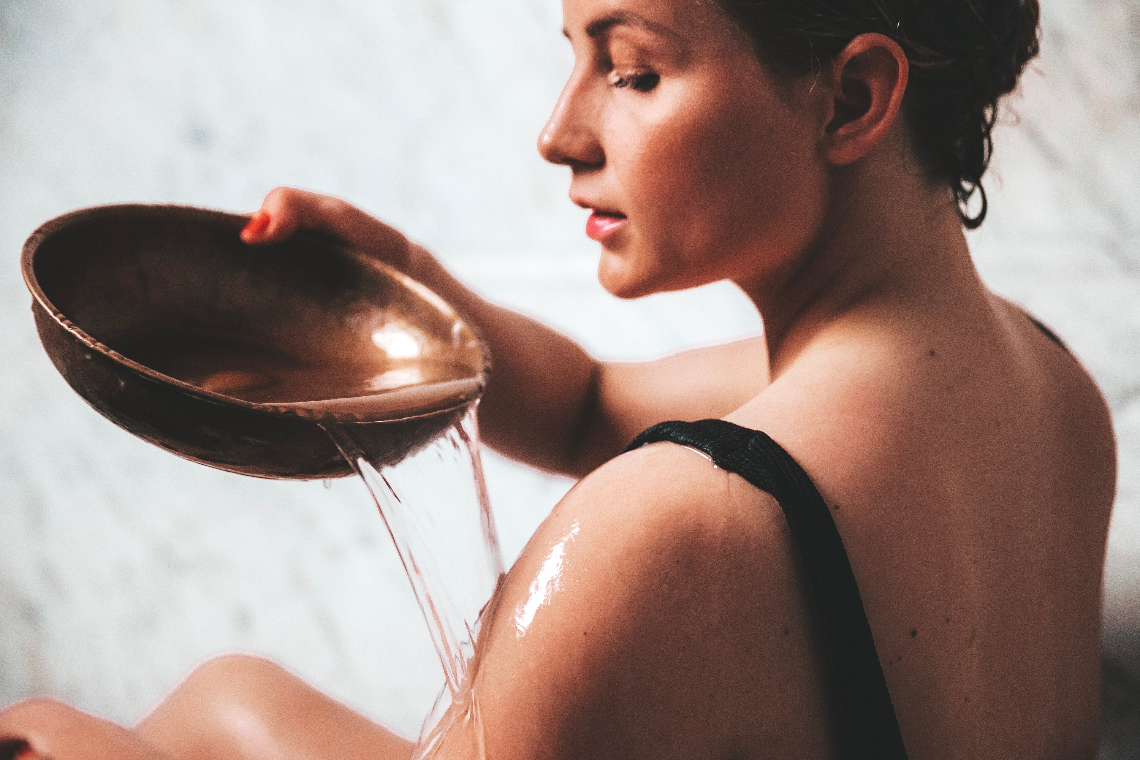 Kvinna öser vatten över sin axel med en rund kopparskål