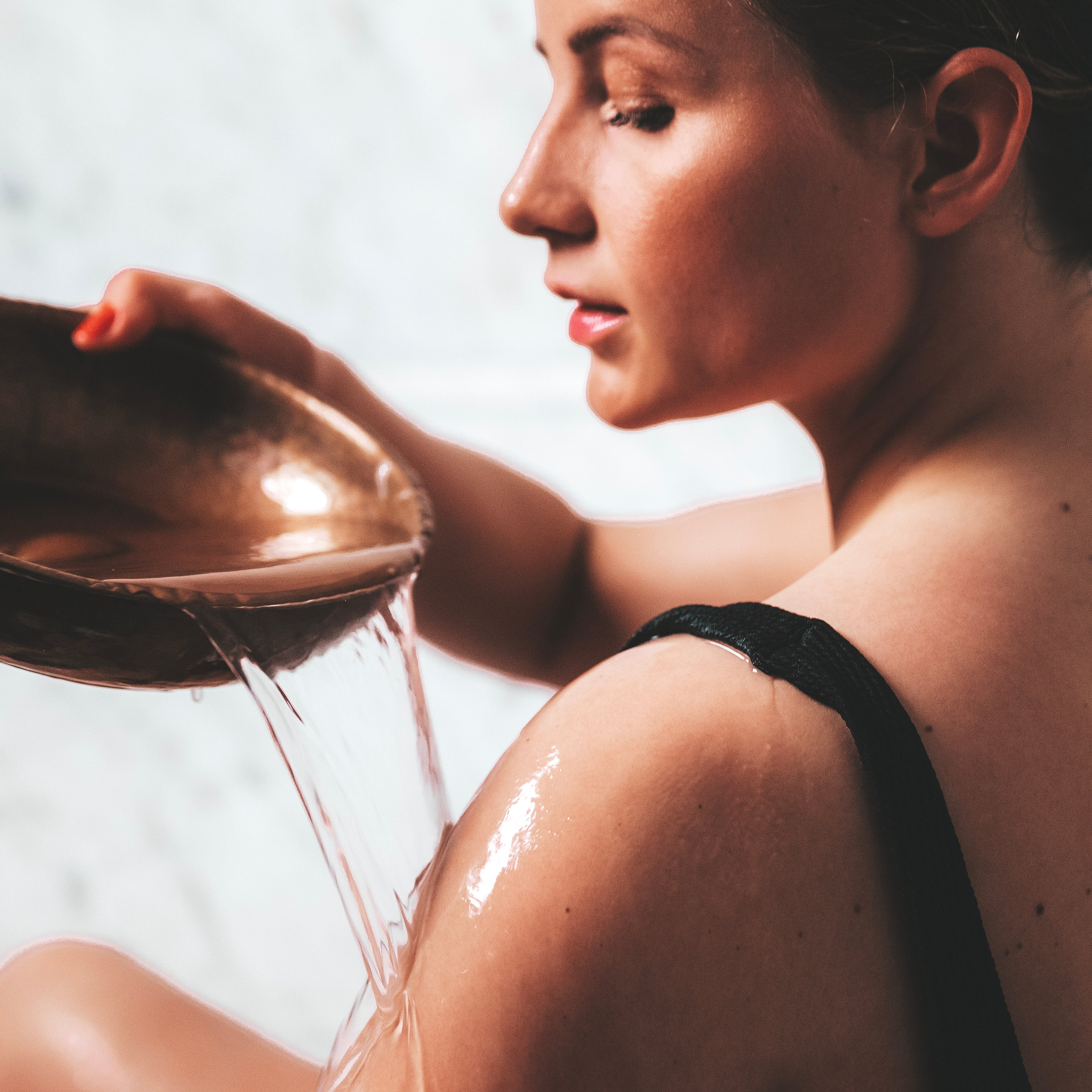 Kvinna öser vatten över sin axel med en rund kopparskål
