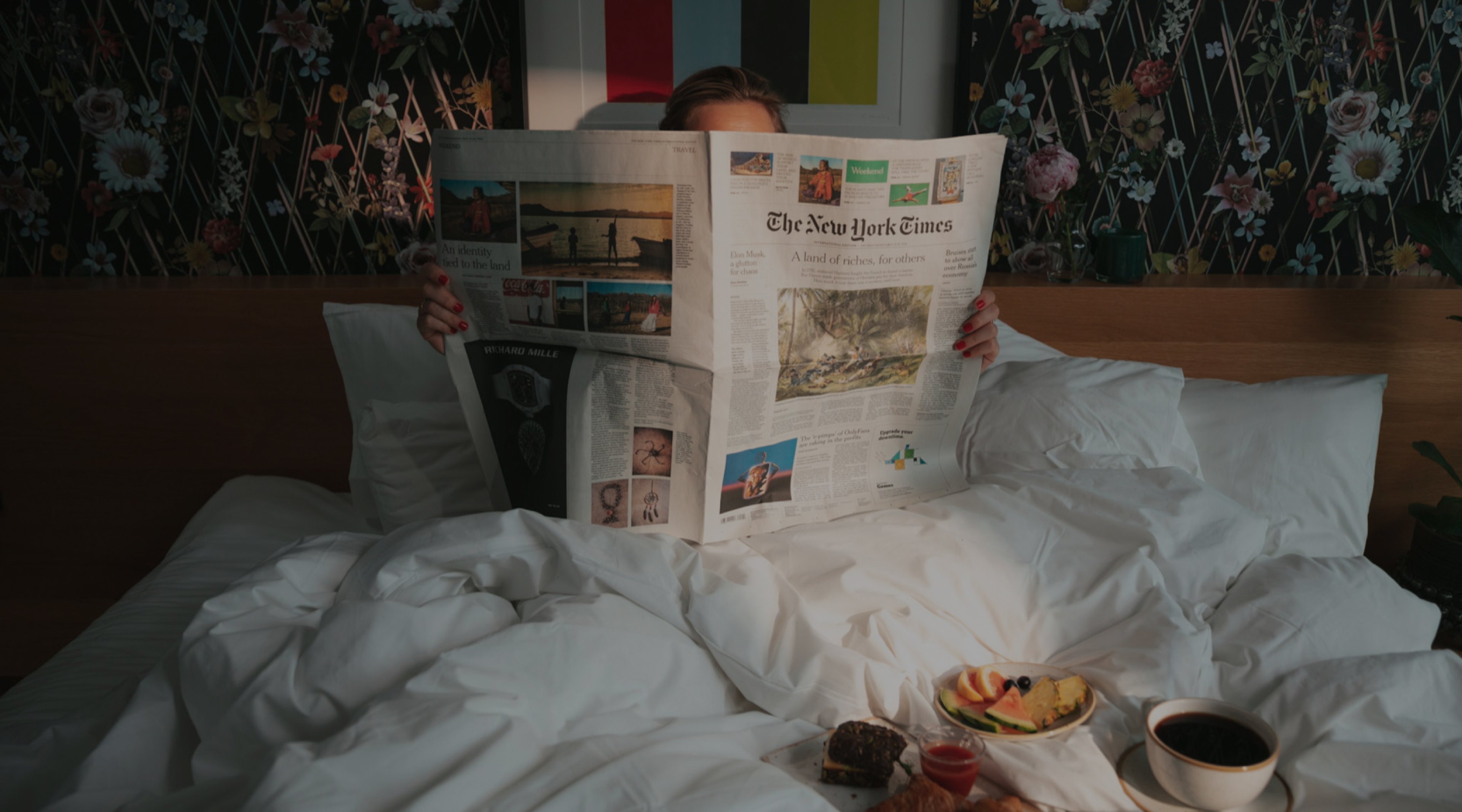 Woman reading newspaper in bed whilst eating breakfast