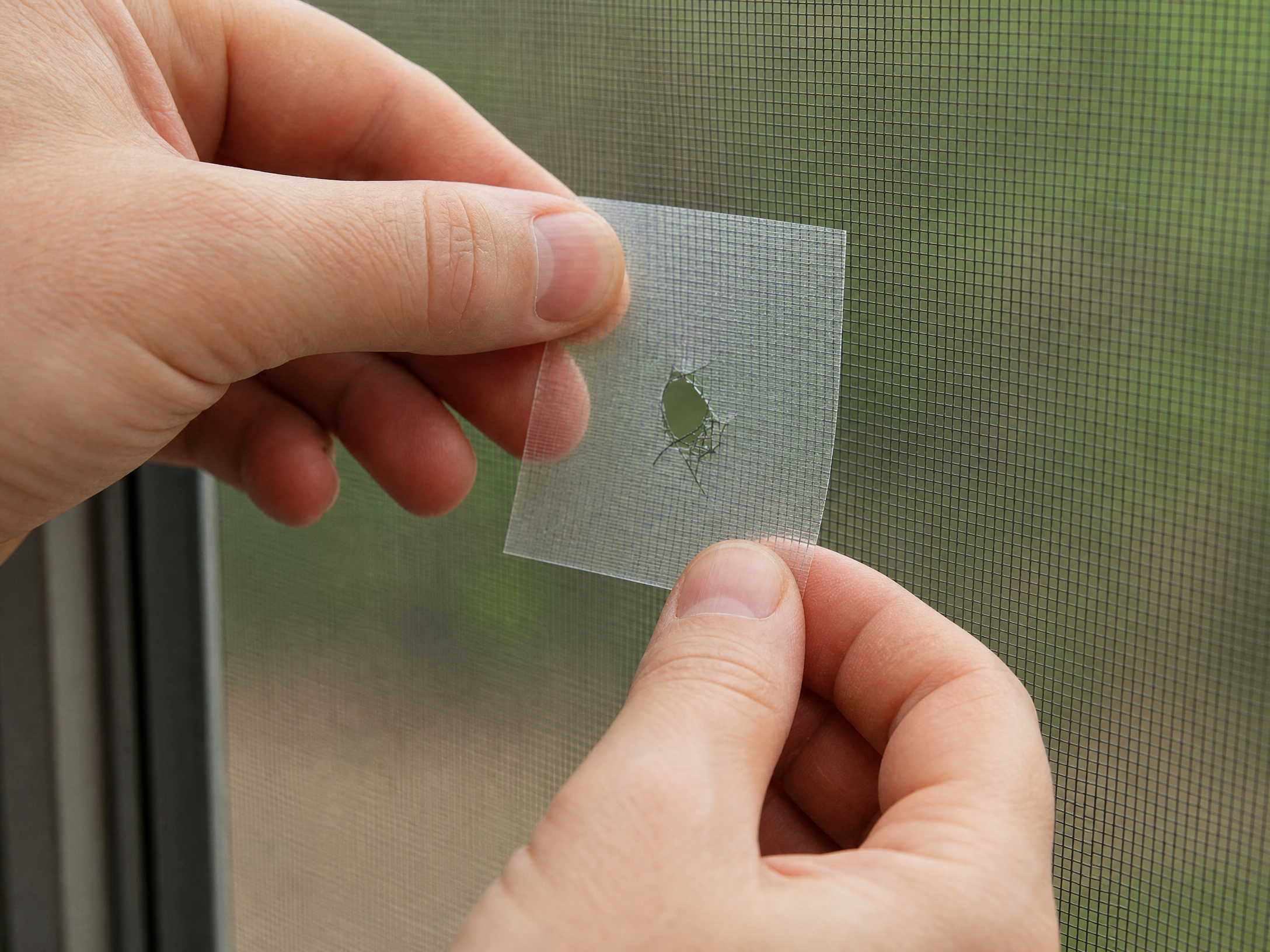 Applying an adhesive screen repair patch to a small hole in window screen mesh
