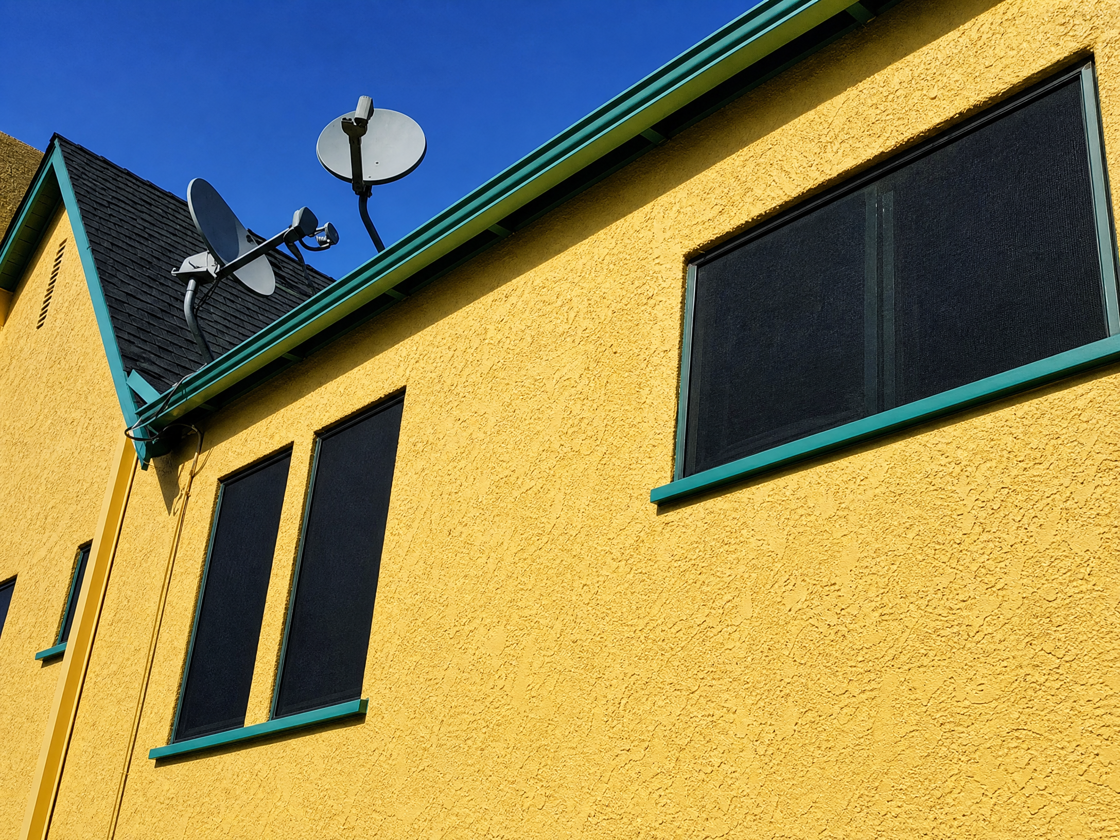 Close-up of yellow stucco building with dark solar screens and teal trim