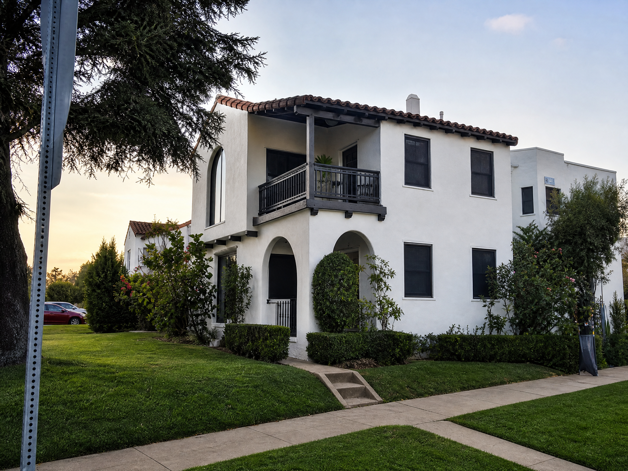 White two-story Spanish-style home with dark solar screens installed at dusk