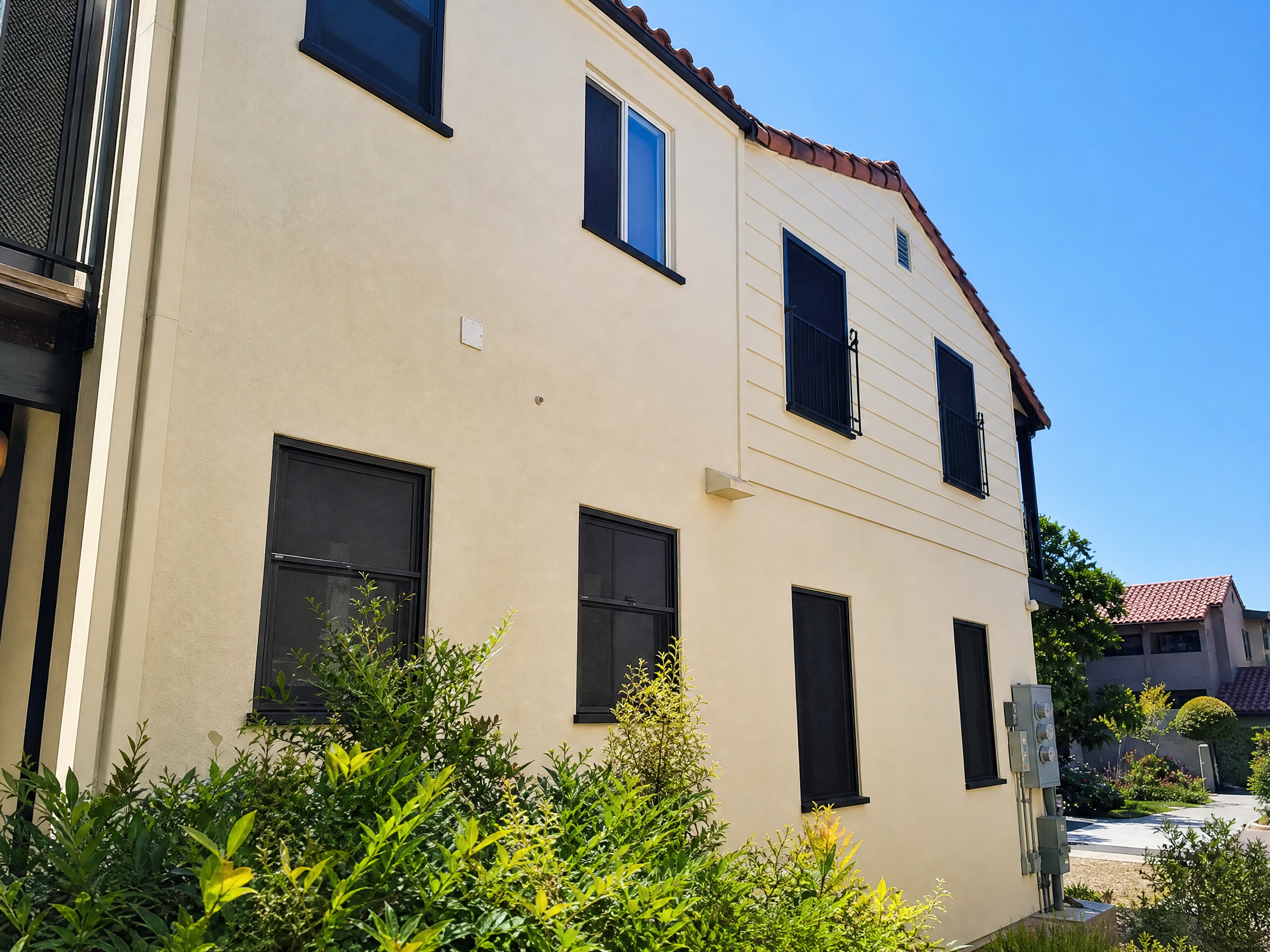 Cream stucco building with black window screens and lush green shrubs