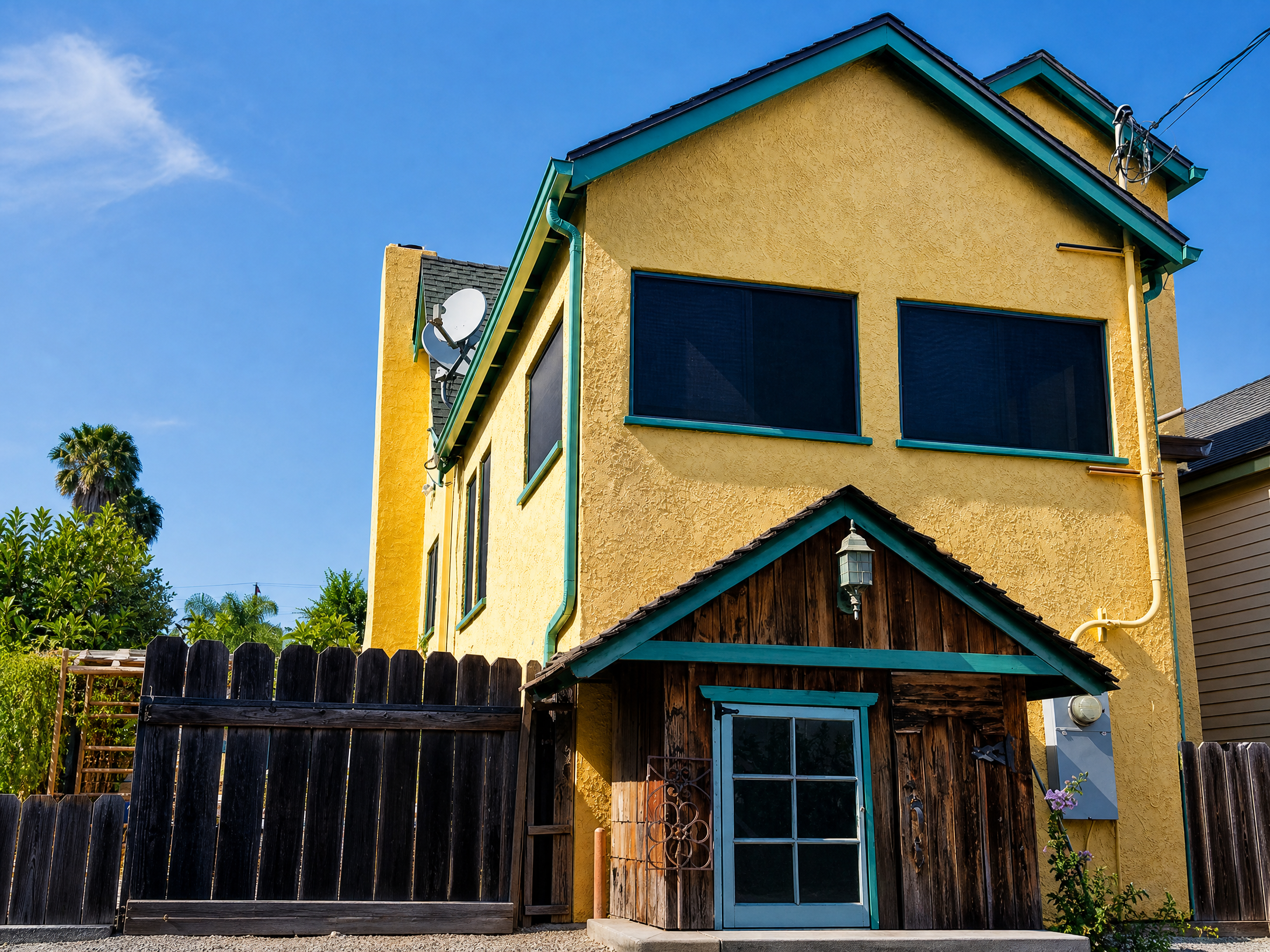 Yellow two-story stucco house with teal trim and dark solar window screens