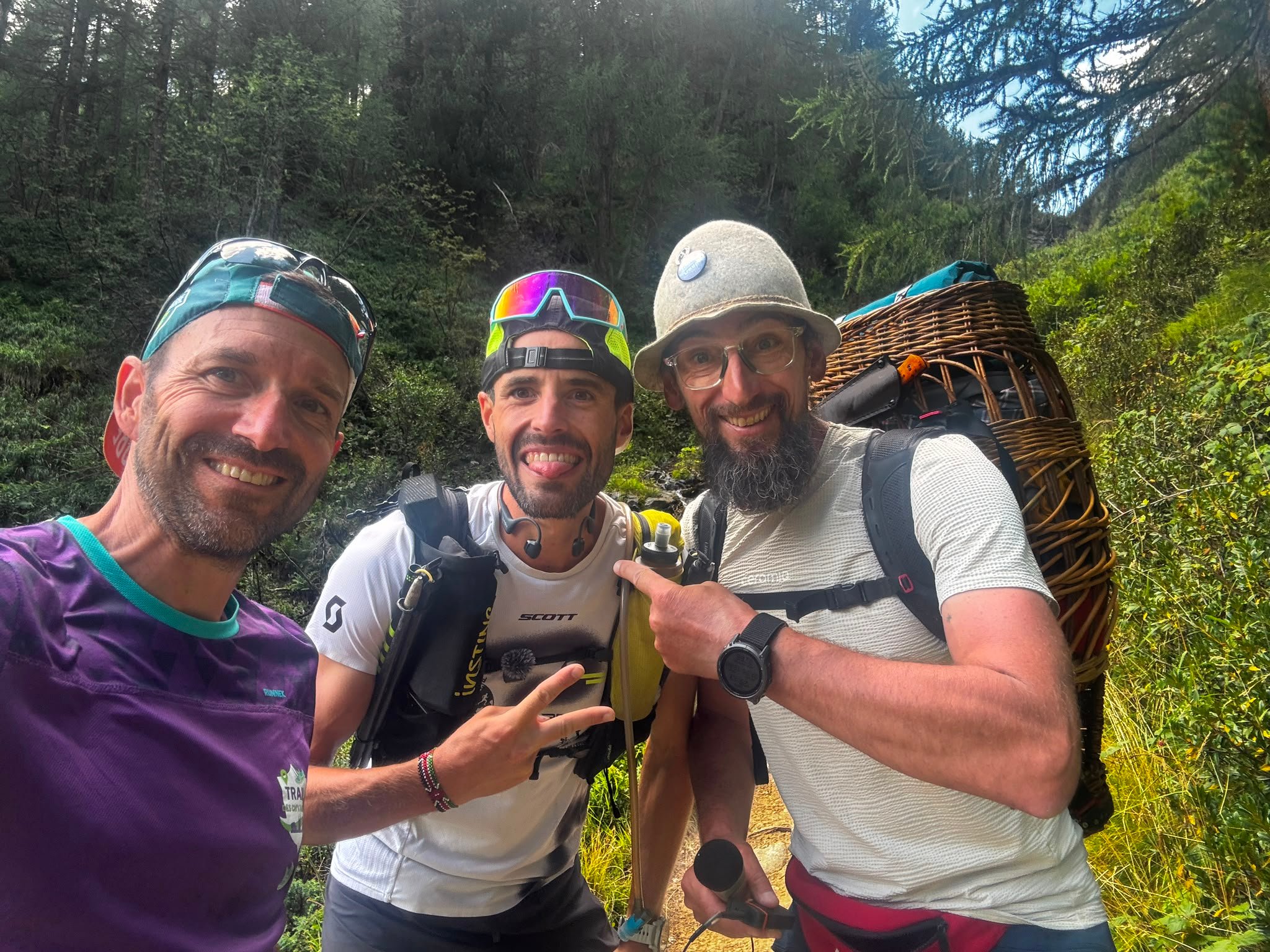 Three men in a trail selfie in a forest, one carrying a wicker basket pack.