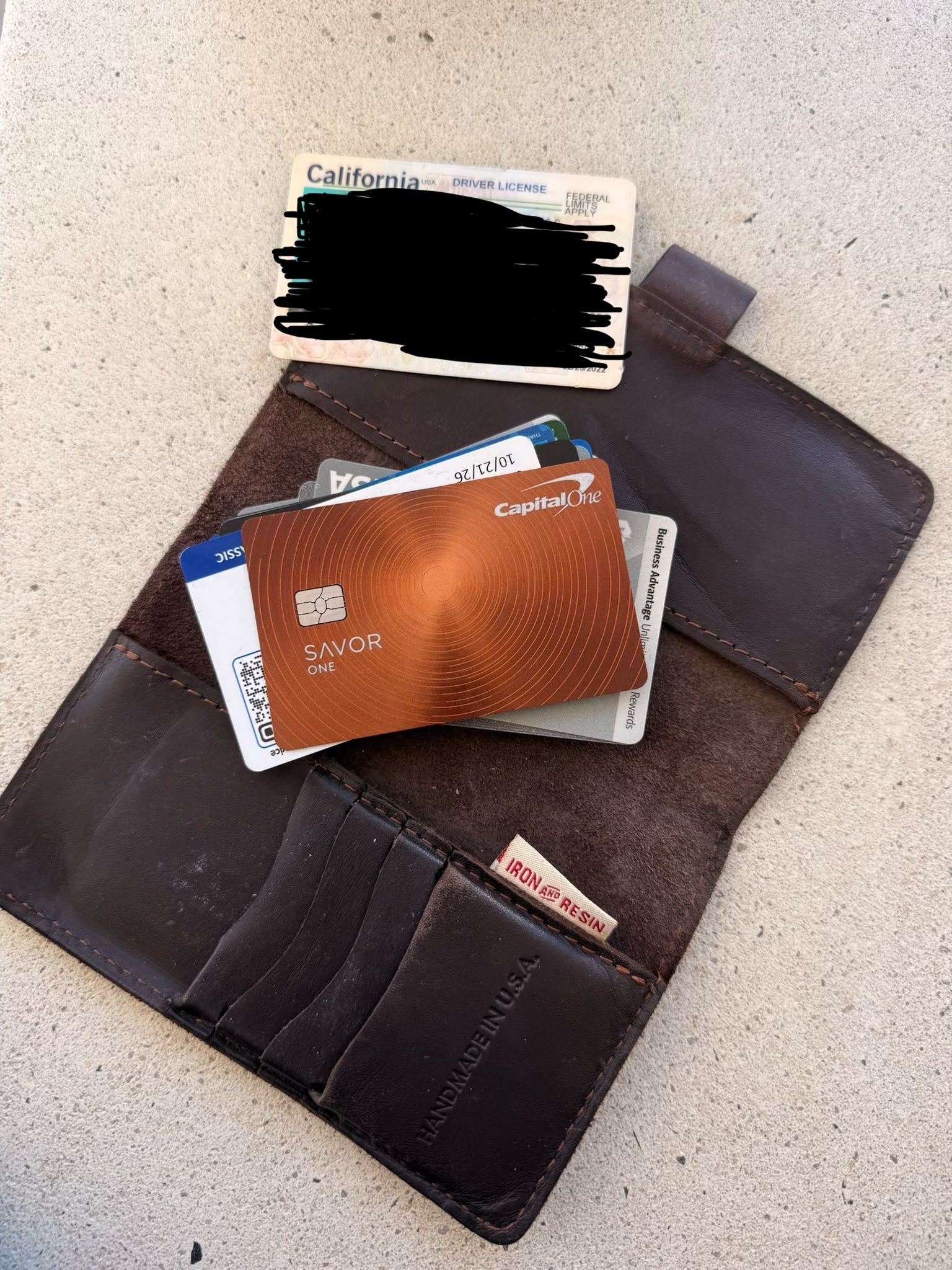 An open brown leather wallet with a California driver licence, blacked out, and bank cards