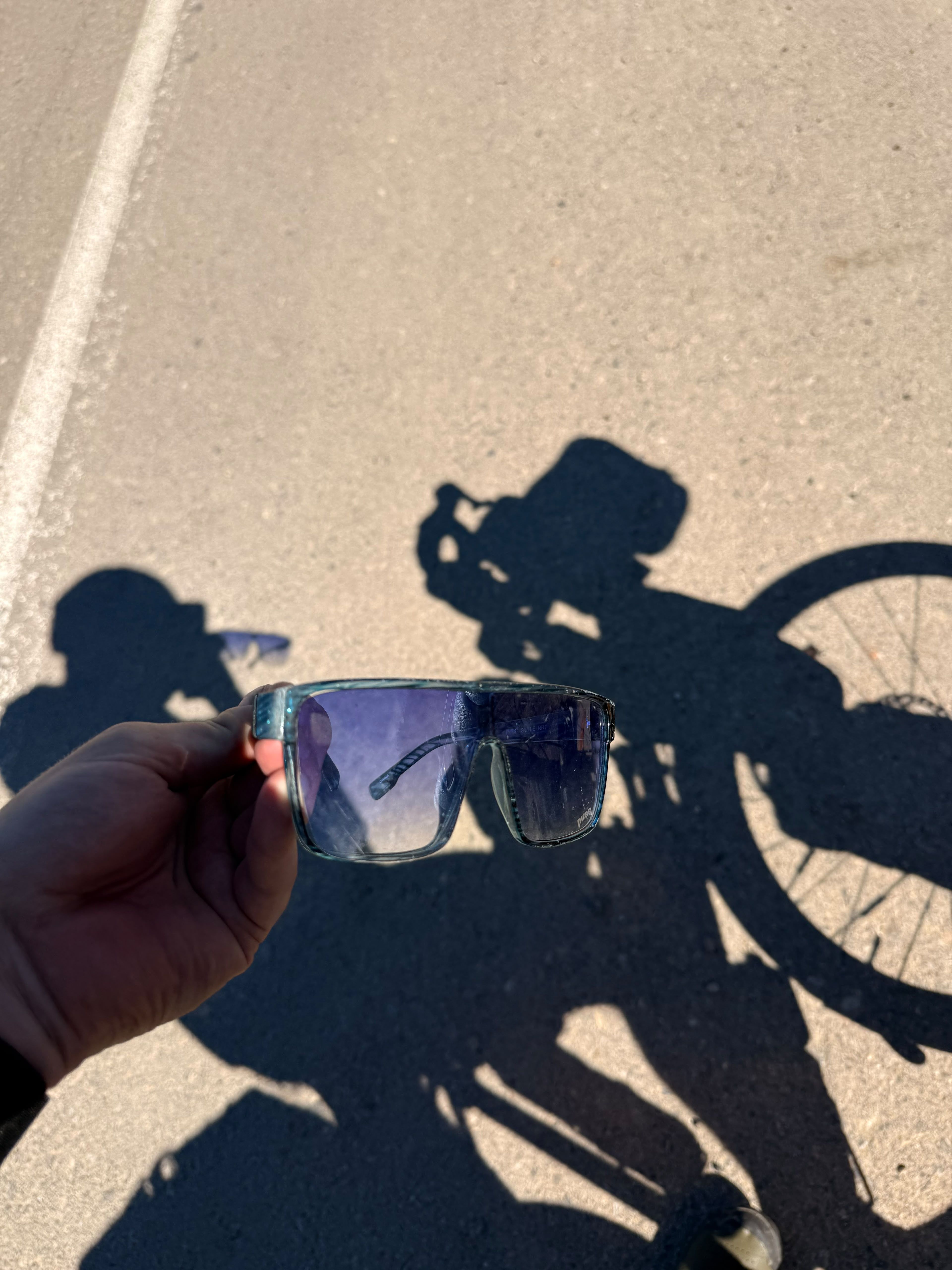 Sunglasses held up against the shadow of a loaded bicycle on the road