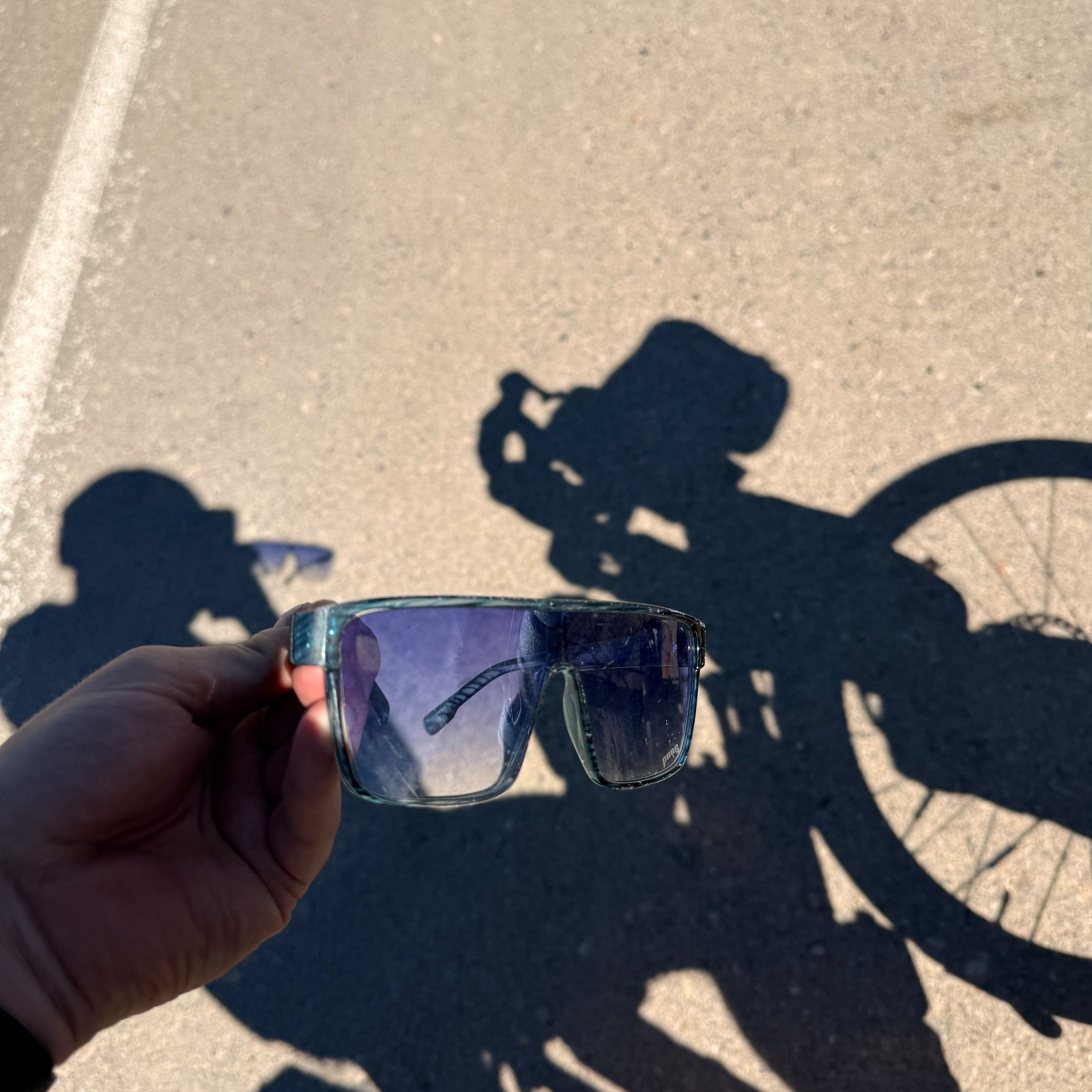 Sunglasses held up against the shadow of a loaded bicycle on the road