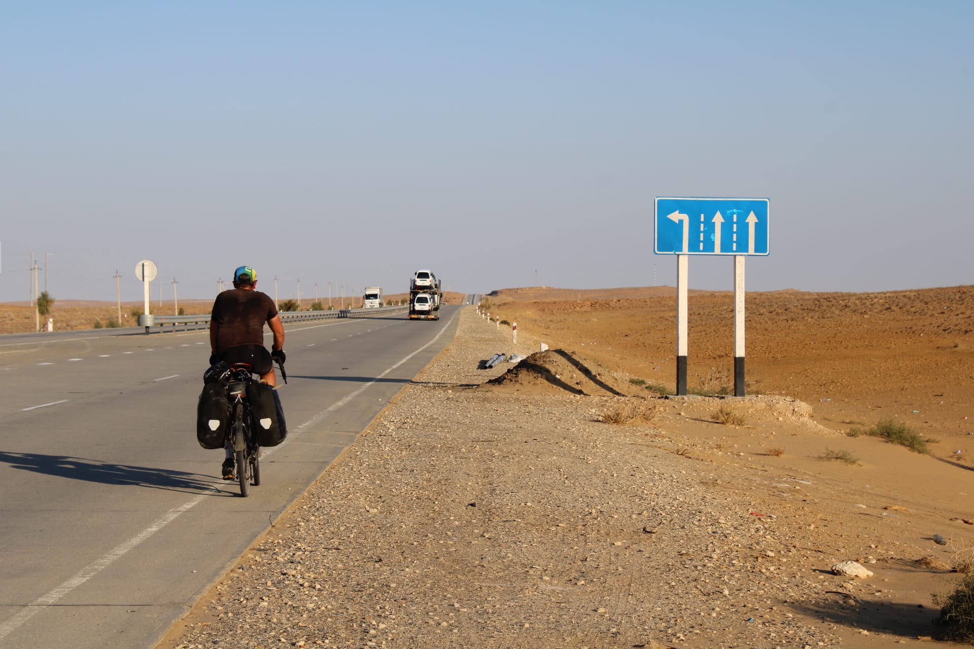 A cyclist with panniers riding away along a desert highway
