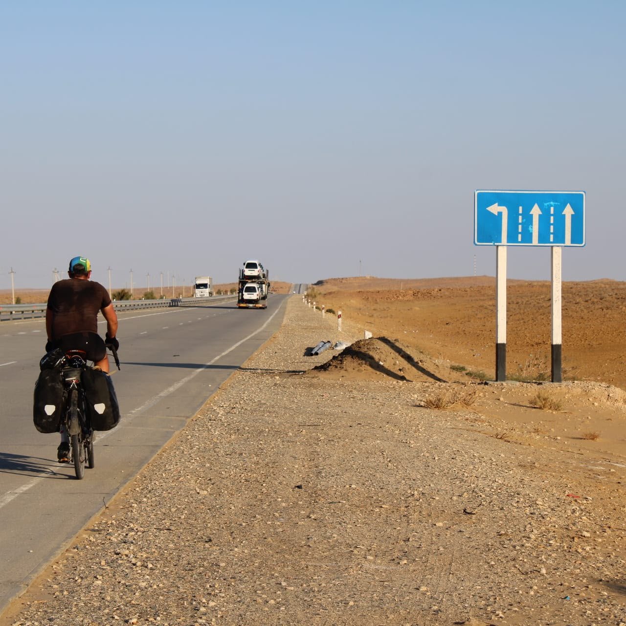 A cyclist with panniers riding away along a desert highway