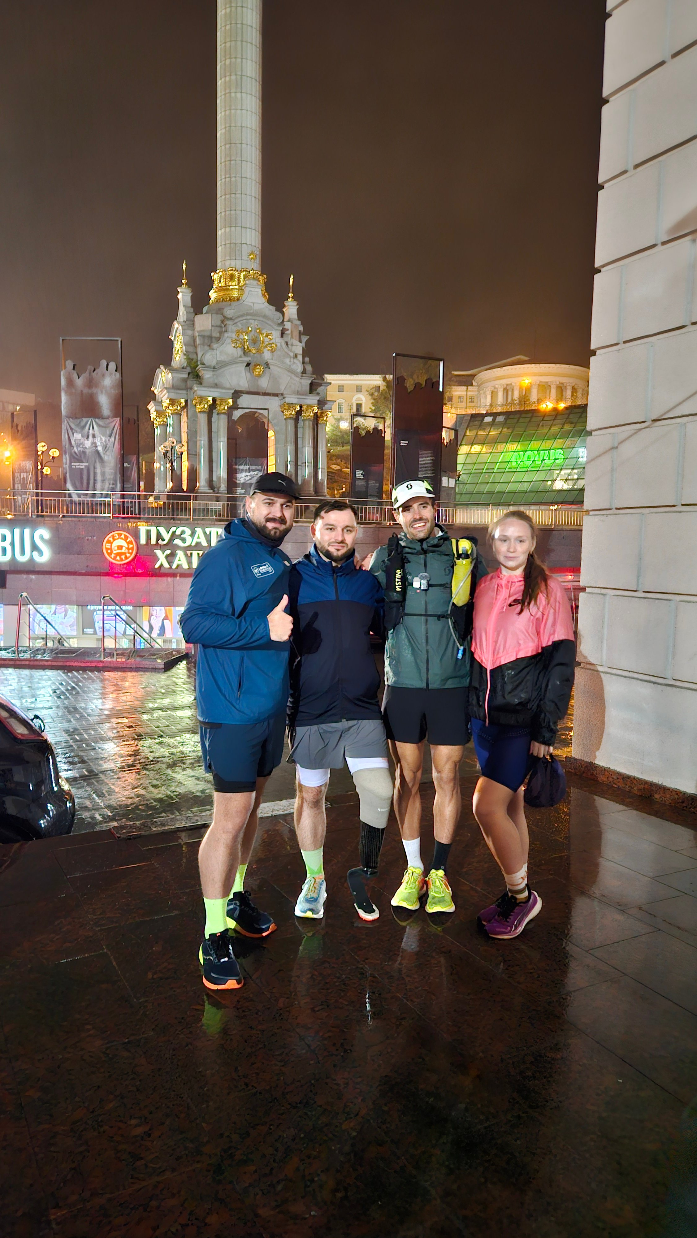 Four people in the rain at night, in front of a lit monument column.