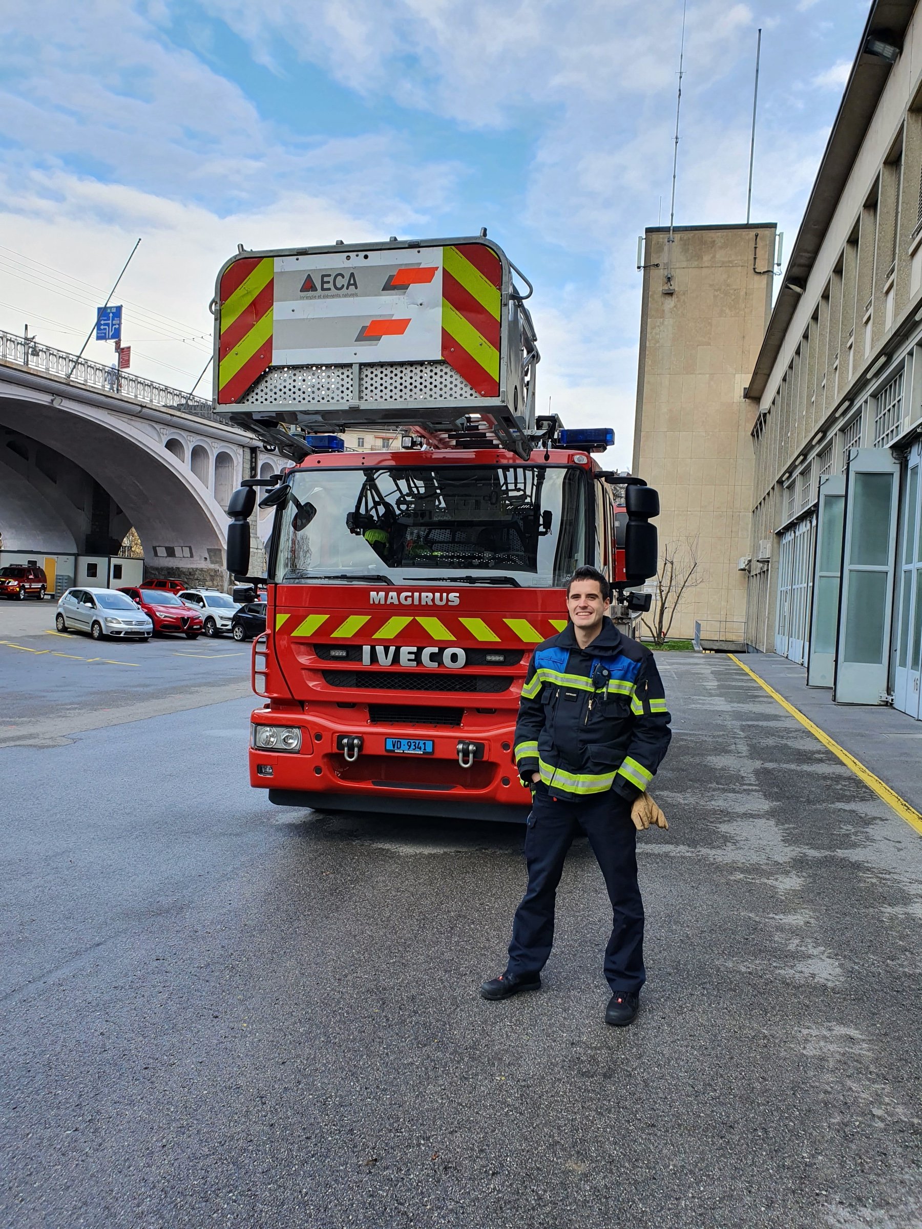 A man in firefighter gear standing in front of a red aerial ladder truck.