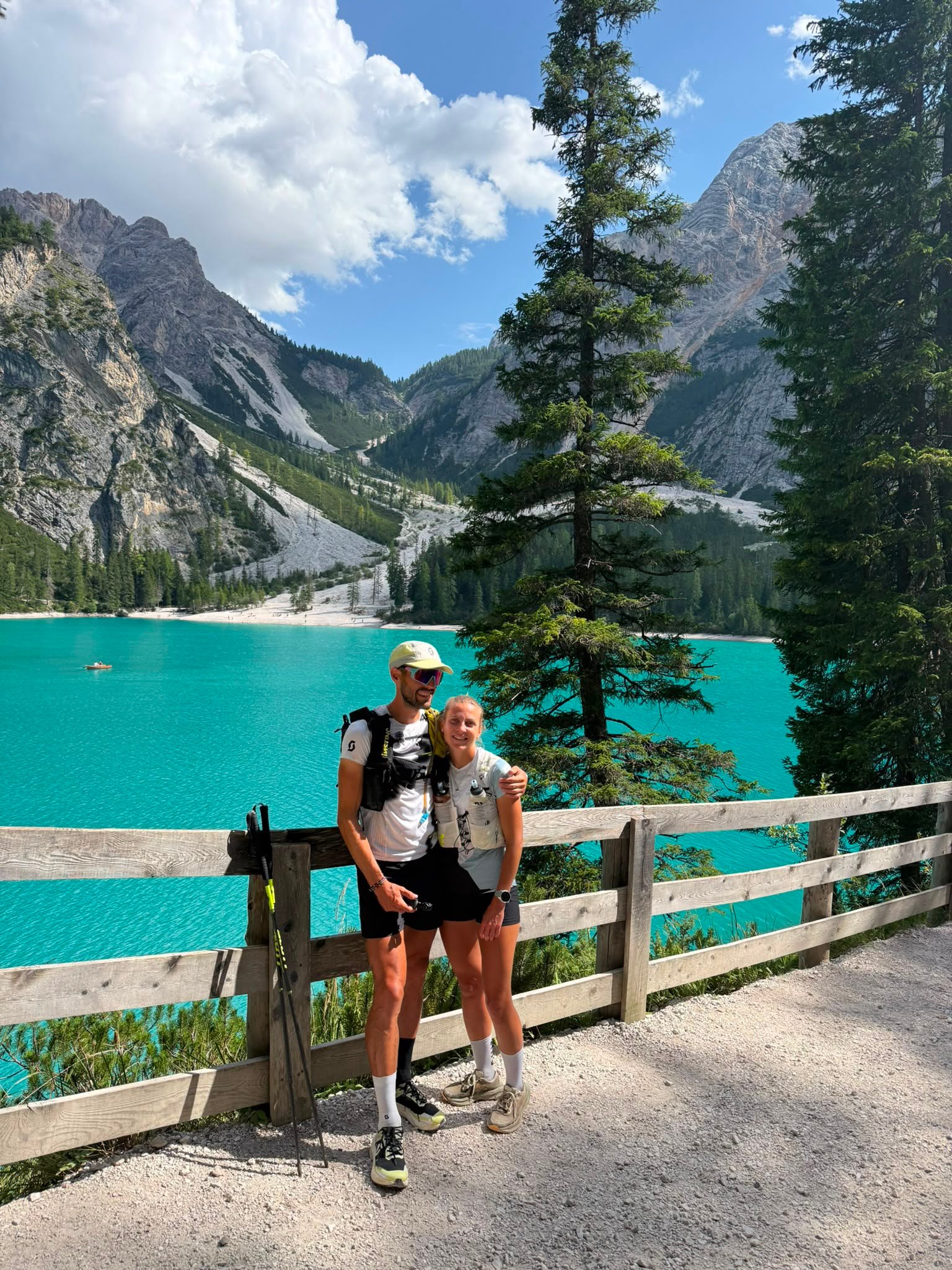A man and a woman posed at a wooden rail above a turquoise lake.