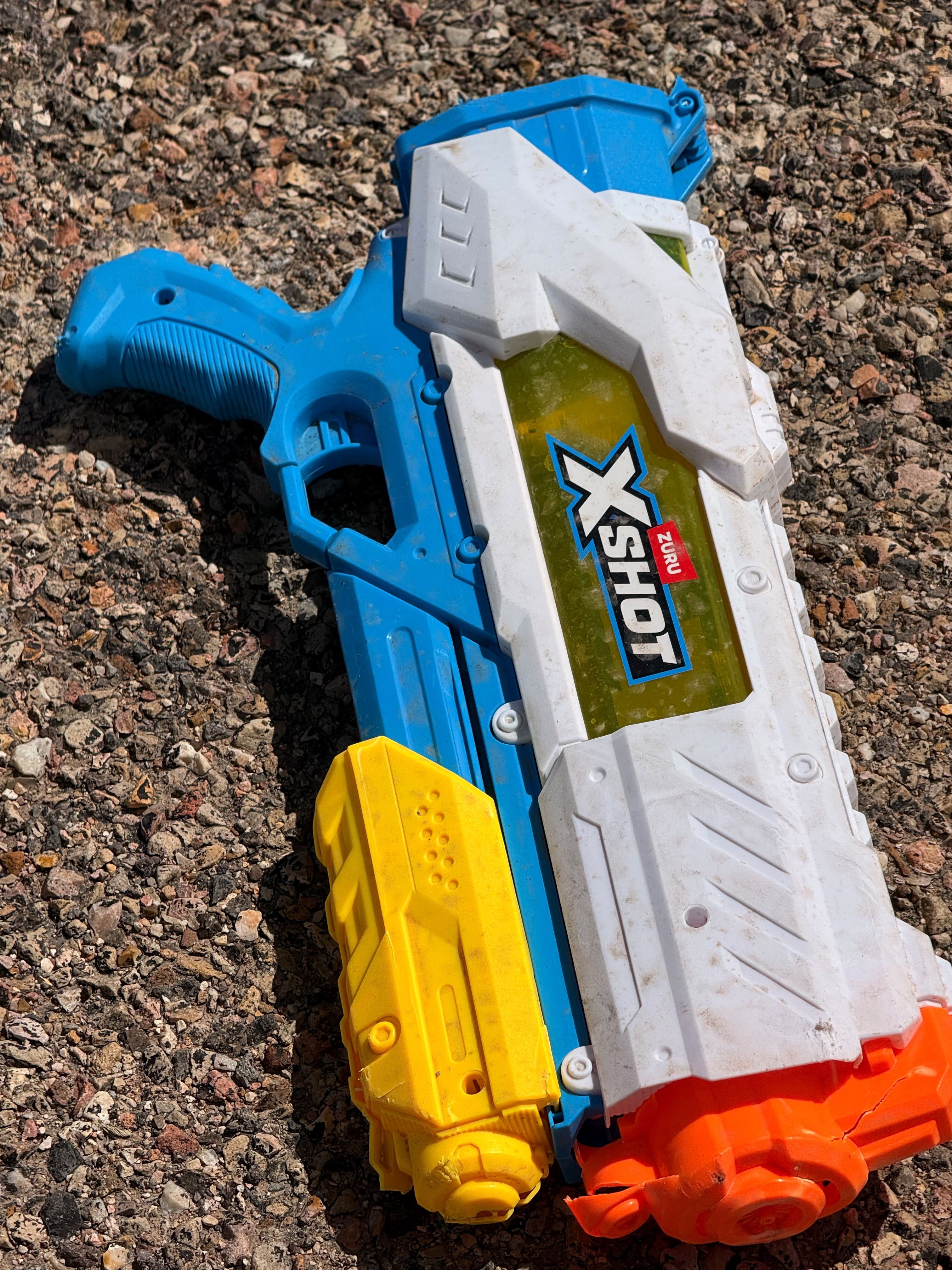 A blue and white toy water gun on gravel