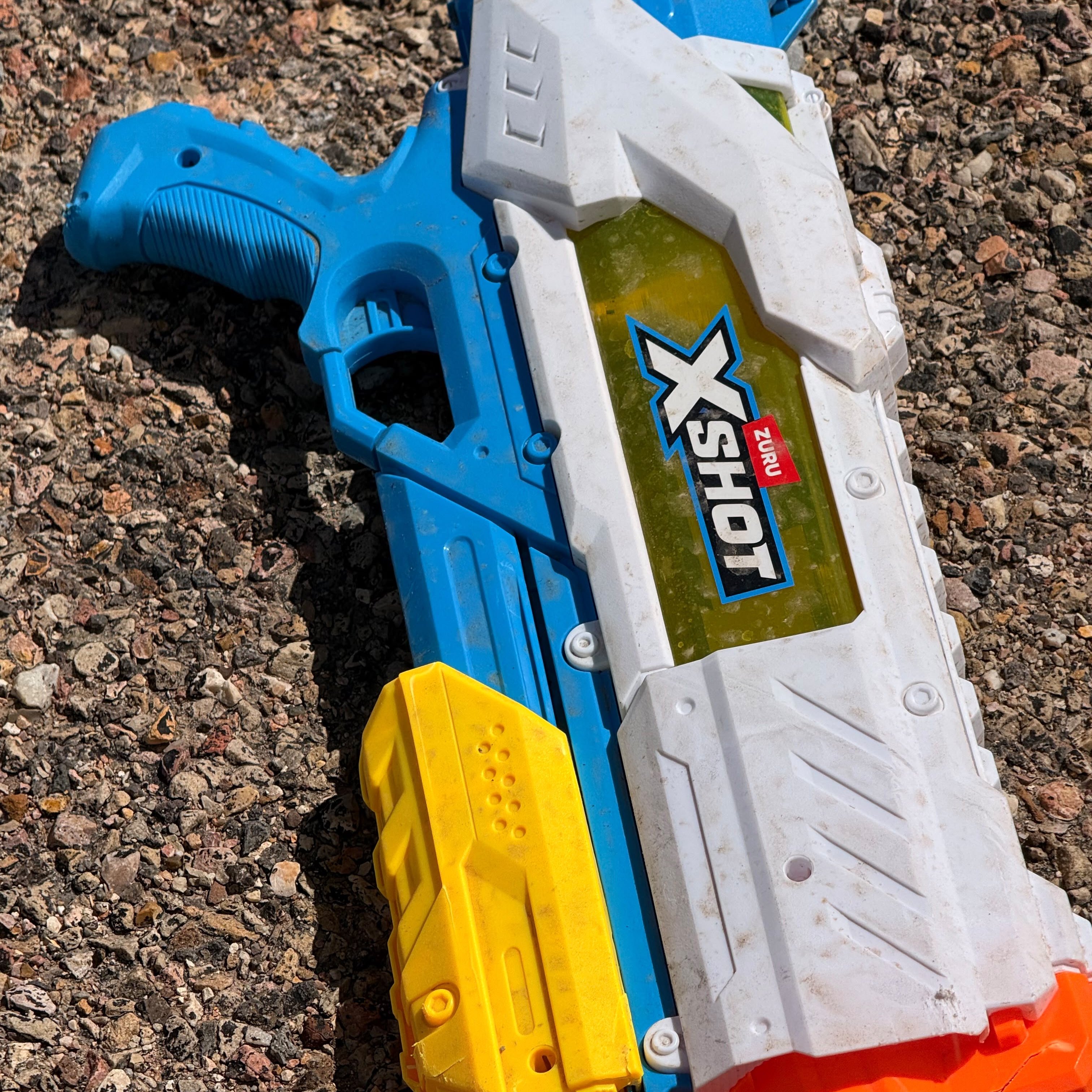 A blue and white toy water gun on gravel