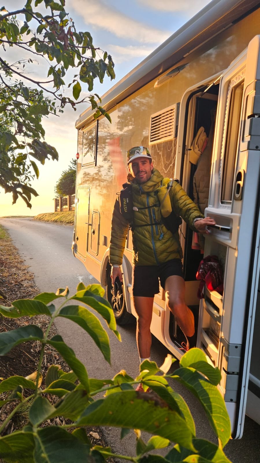 A man in a puffer jacket and running vest stepping out of a camper van door in golden light.