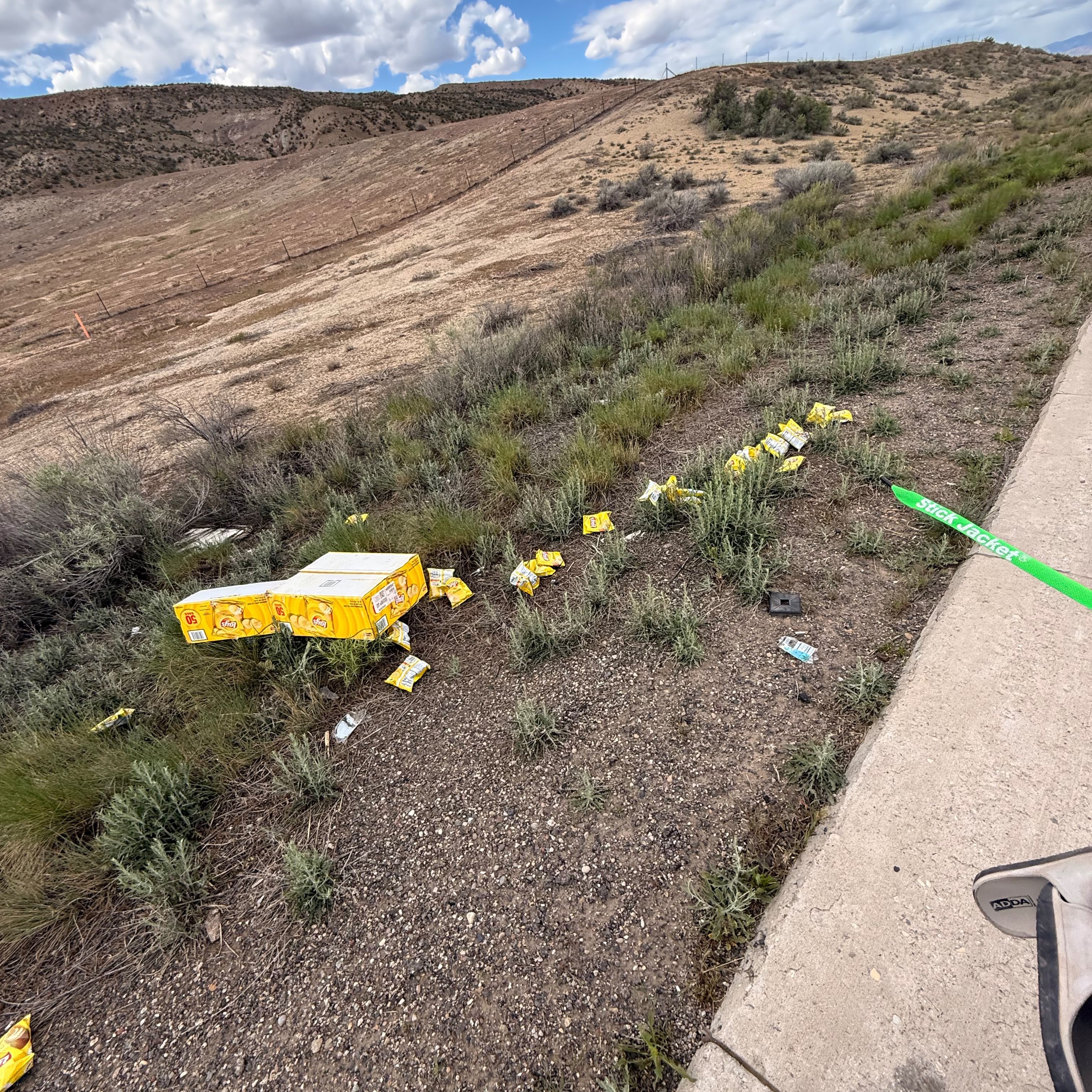 Boxes of crisps scattered up a hillside beside the road