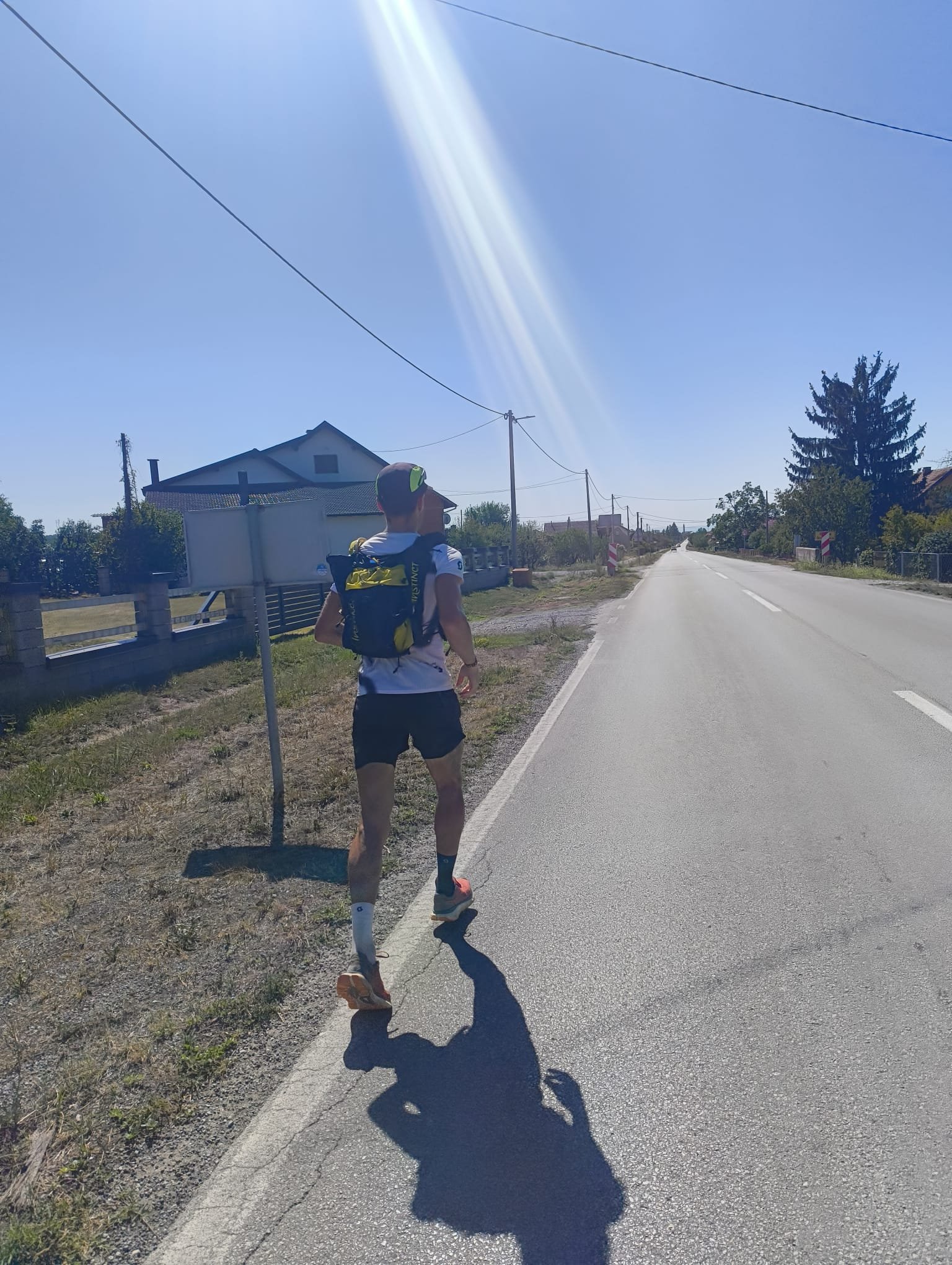 A runner seen from behind on a sunny village road with lens flare.