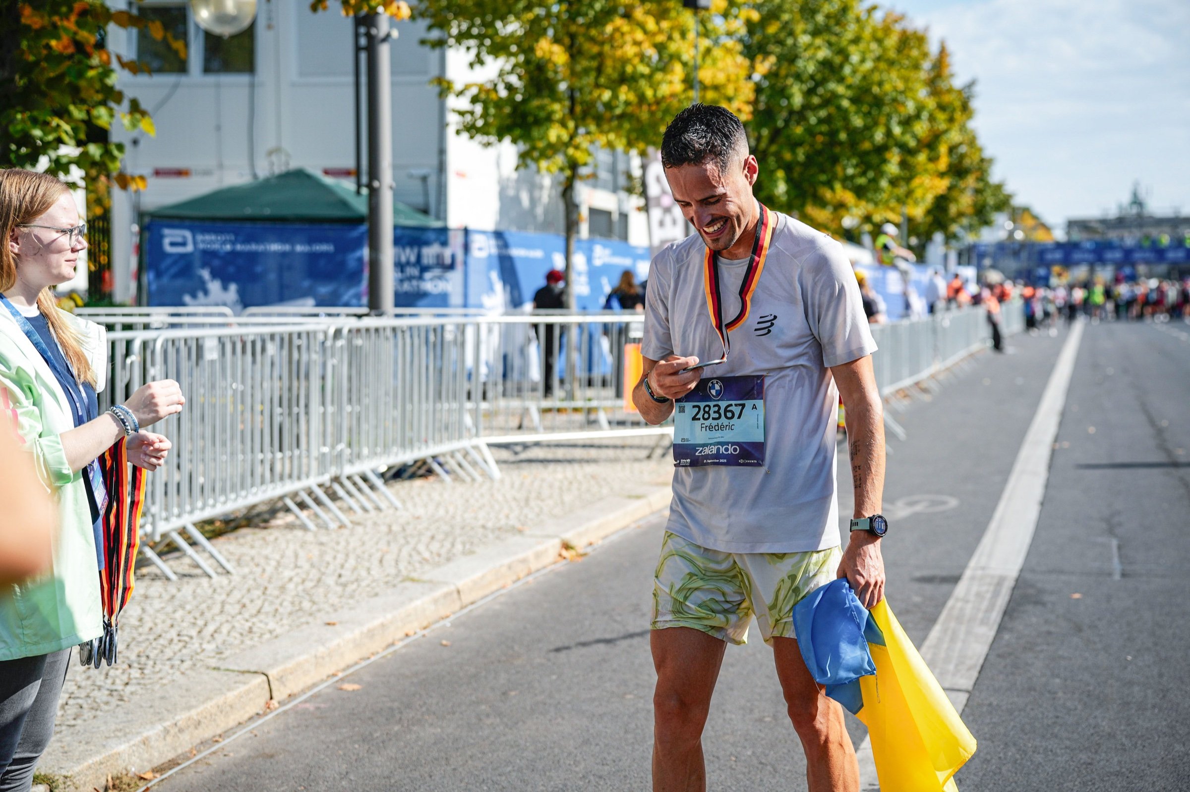 Frédéric smiling after a marathon, a medal ribbon around his neck and a blue and yellow flag in his hand.