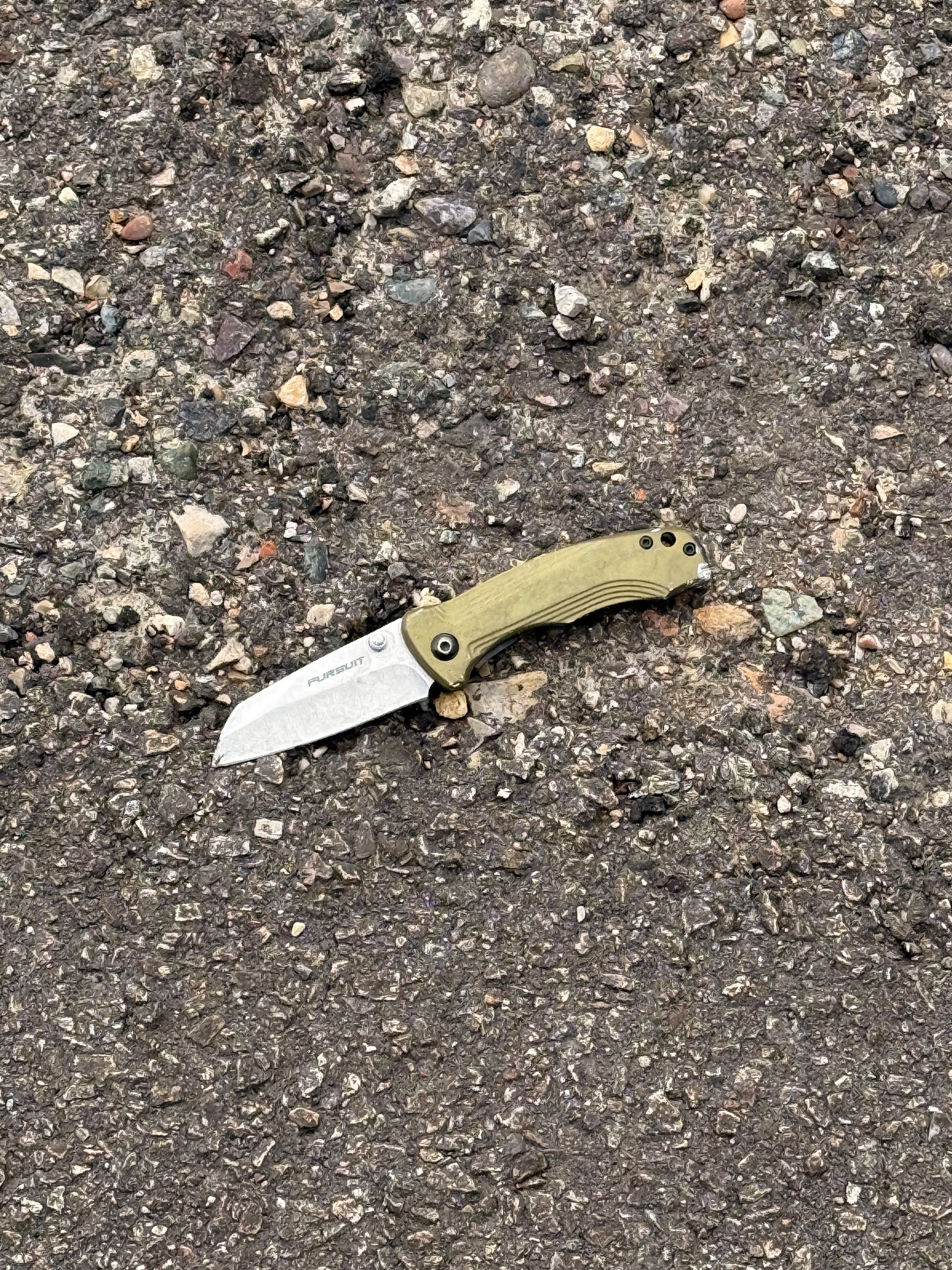 A folding knife with a green handle on asphalt