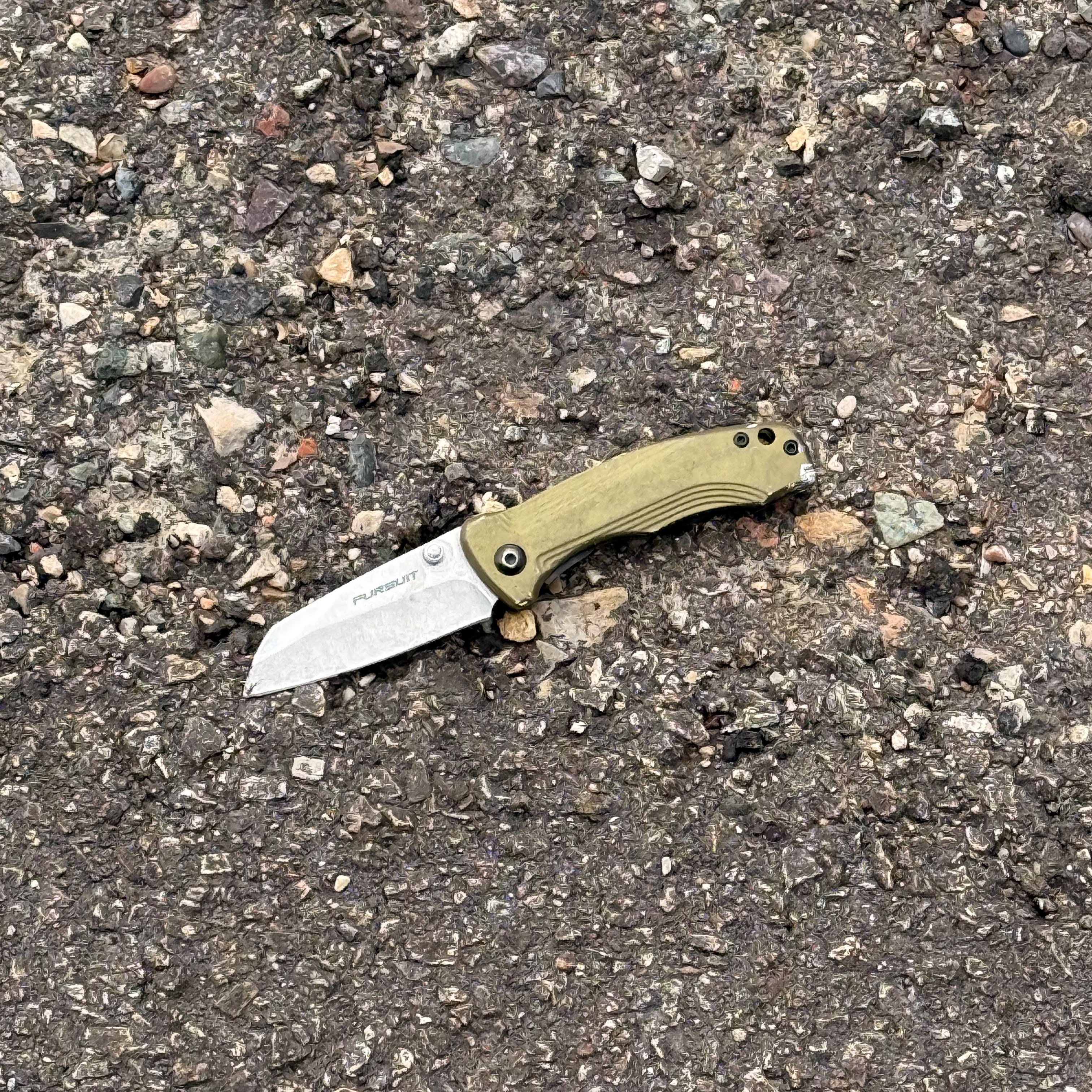 A folding knife with a green handle on asphalt