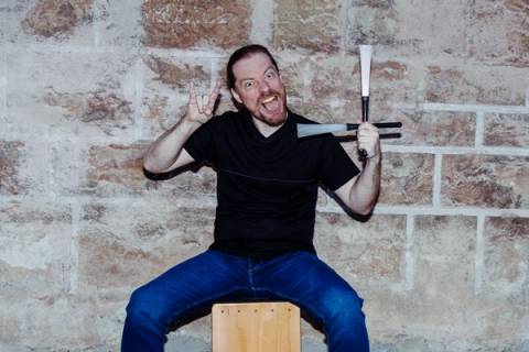 Percussionist auf dem Cajón mit Schlägeln, grimassierend vor der Steinmauer
