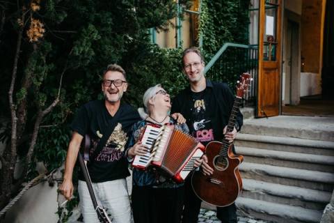 Drei Bandmitglieder lachen gemeinsam, mit Akkordeon und Gitarre