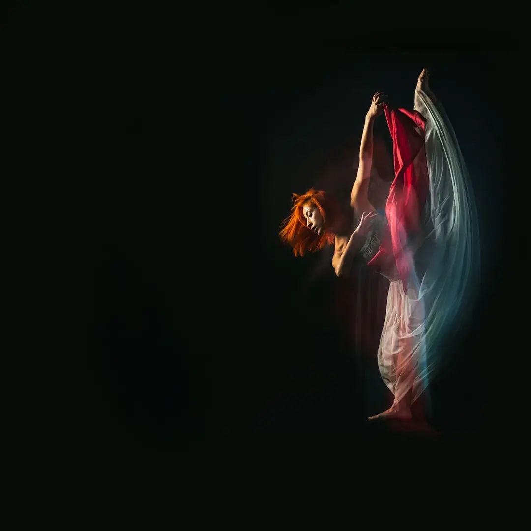 A dancer mid-turn with red fabric in motion against a black background