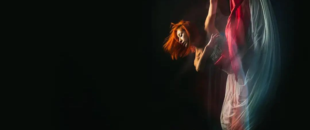 A dancer mid-turn with red fabric in motion against a black background