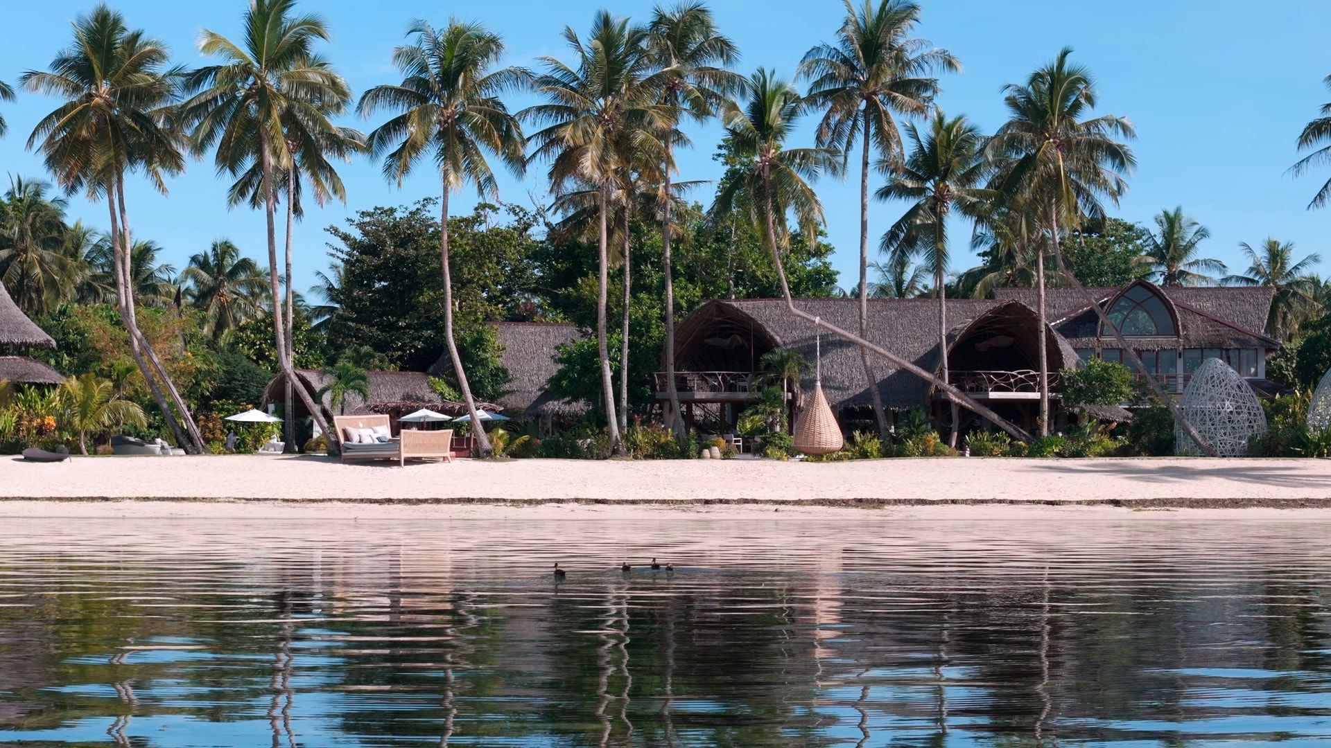 The resort seen from the water: villas and palm trees behind a white beach