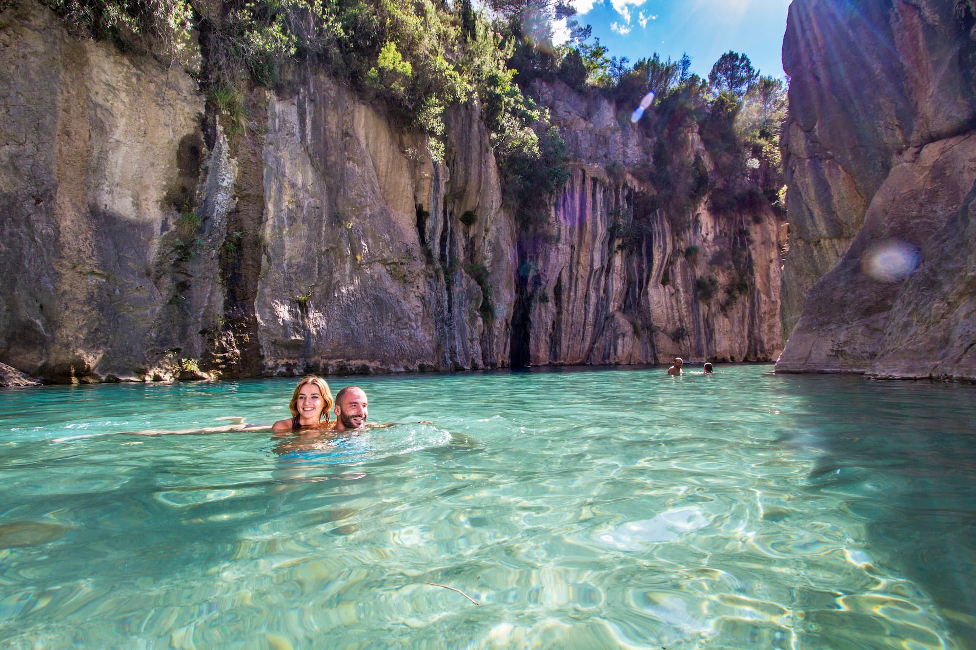 Bathers in a turquoise river pool between limestone cliffs