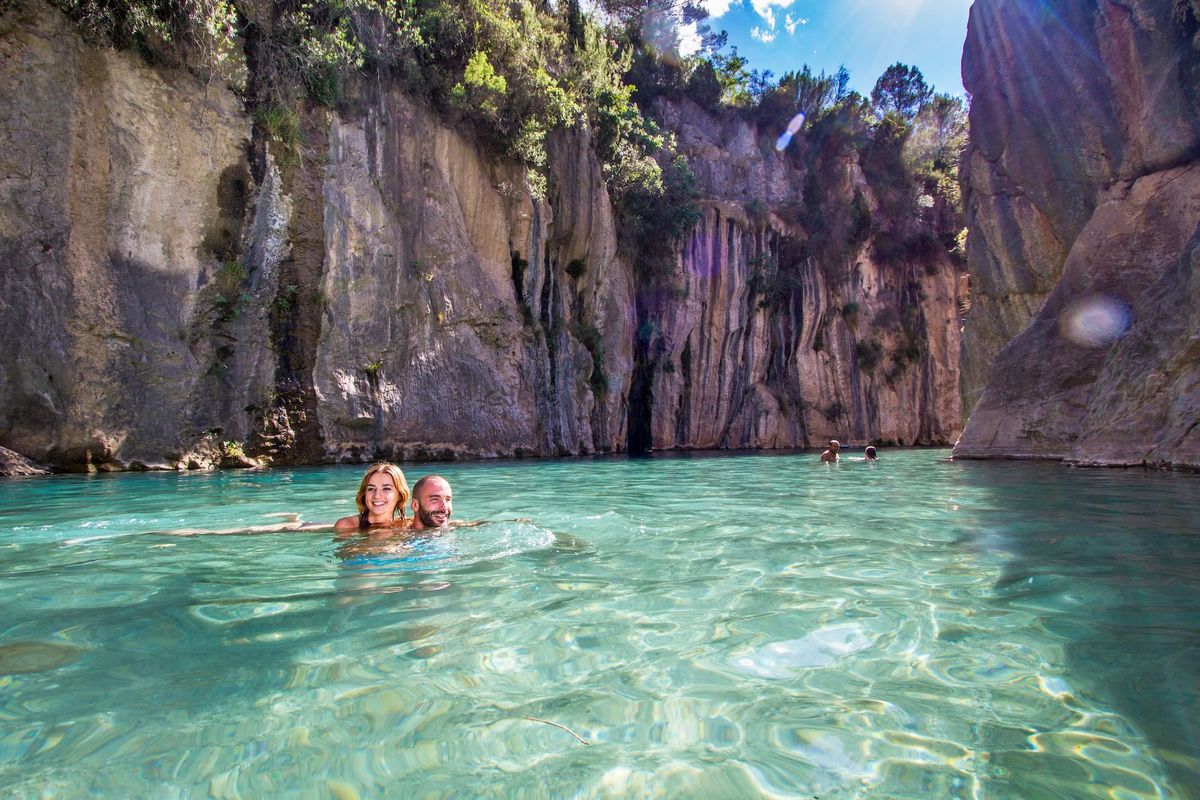Bathers in a turquoise river pool between limestone cliffs