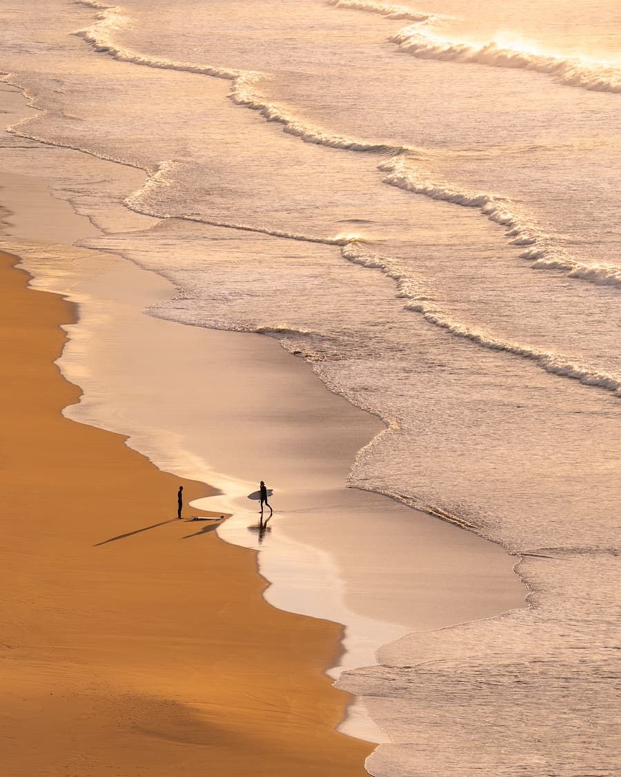 Two people walking along a golden shoreline, seen from above. Photo by @desigraphie