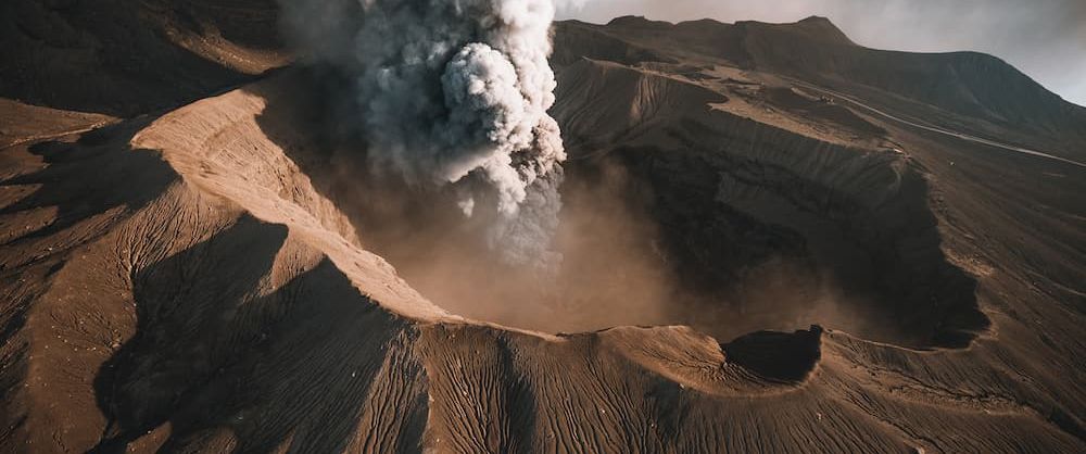 Aerial view of an erupting volcano crater. Photo by @muenchmax