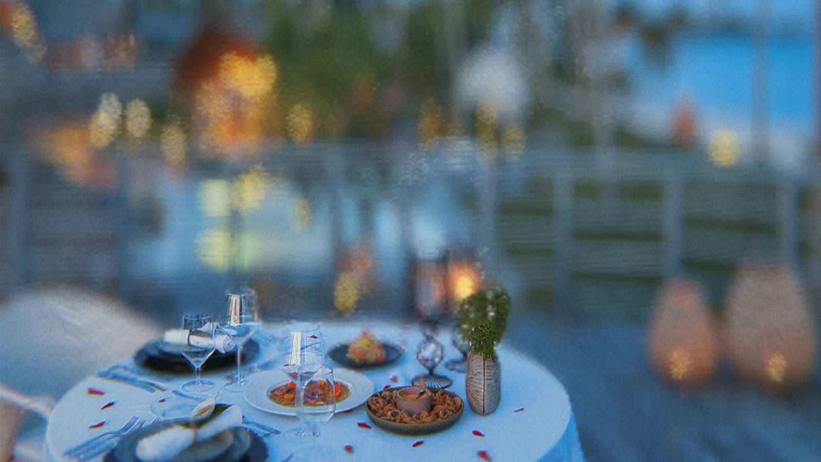 A table set for dinner on a deck at dusk, in focus, with the resort lights melting into discs of light behind it