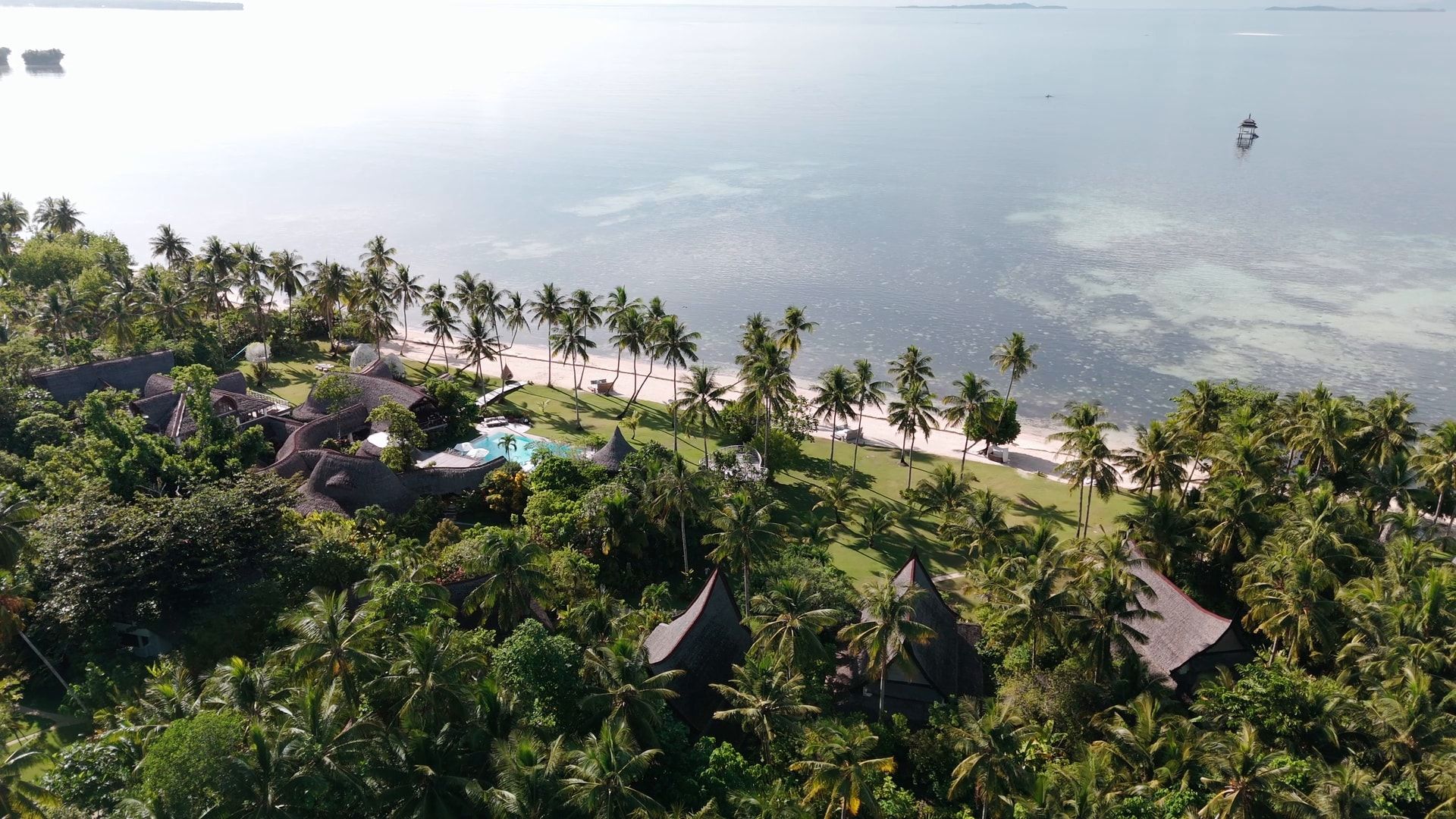 Drone shot over thatched villas among palm trees, towards the beach