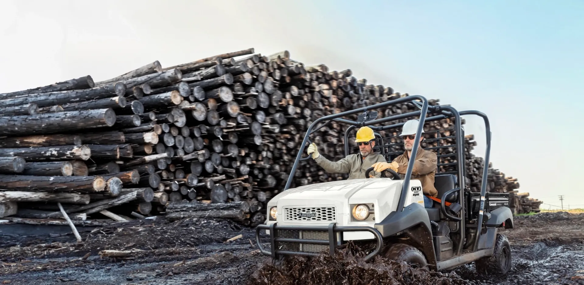 Two men in a Kawasaki UTV on a work site near logs.