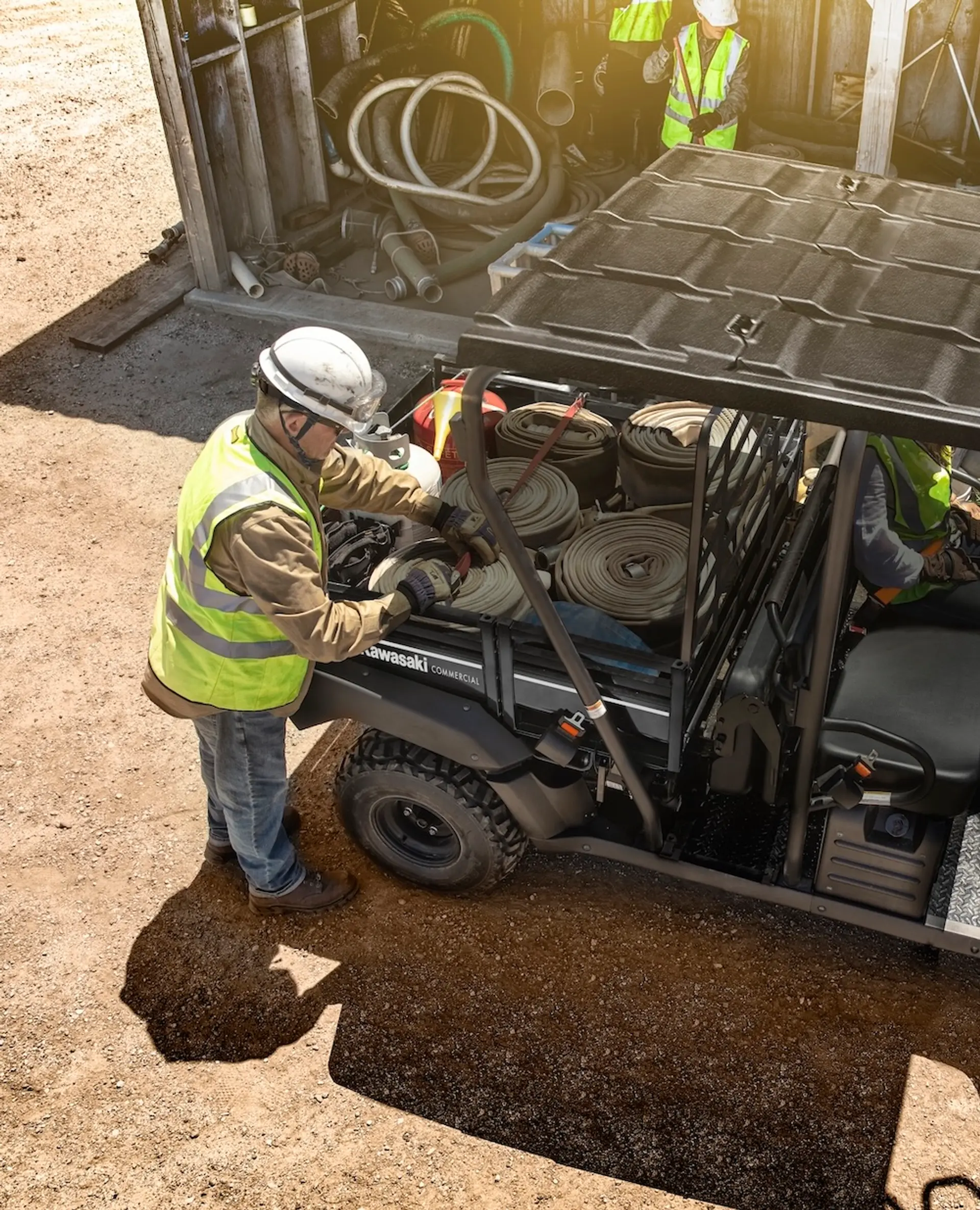 Two men on a work site next to the bed of a Kawasaki UTV.