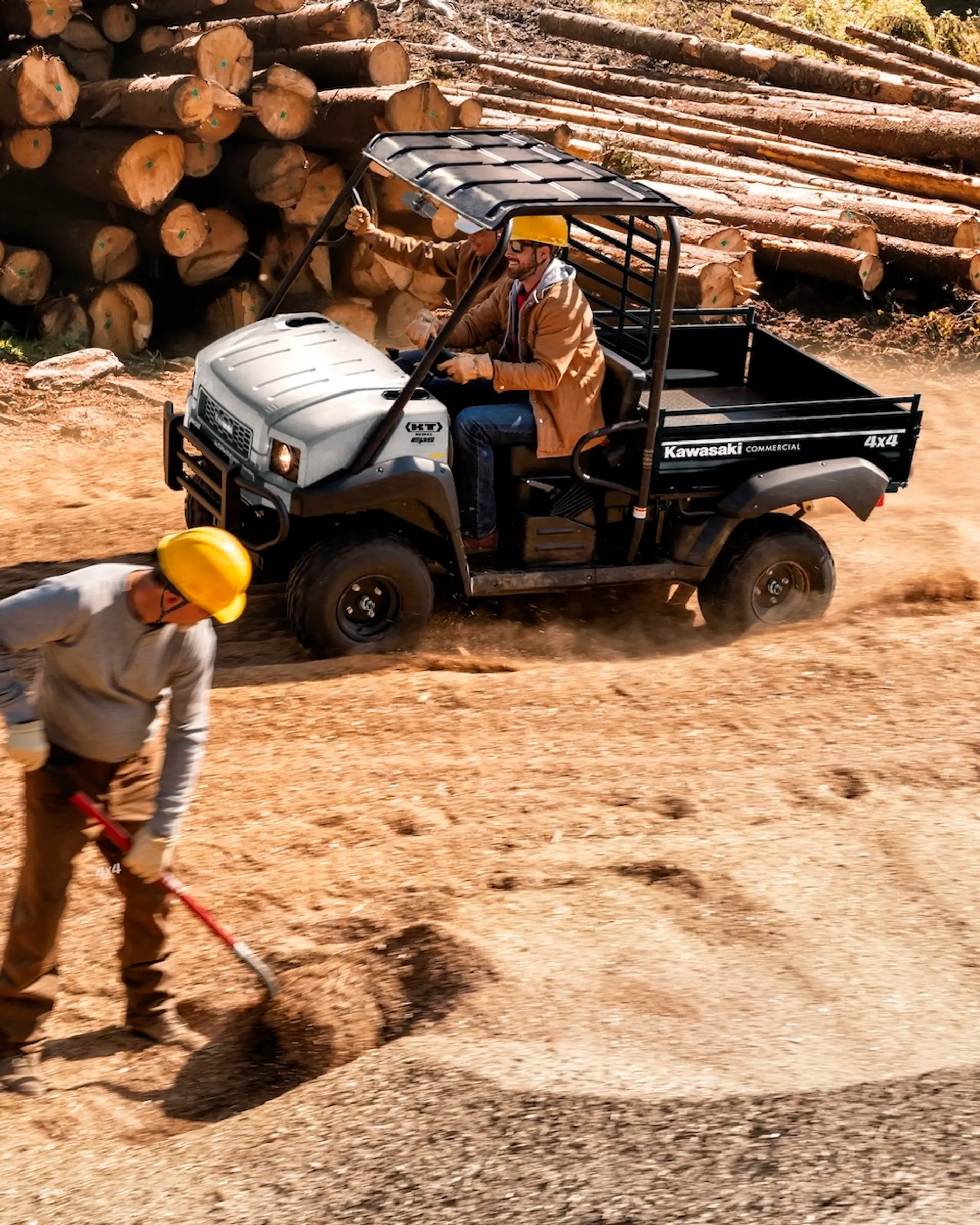 A Kawasaki UTV driving next to a pile of timber.