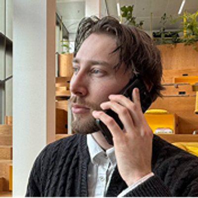 Portretfoto van Milo van Sluis die aan het bellen is in een moderne kantooromgeving met warme houten elementen.