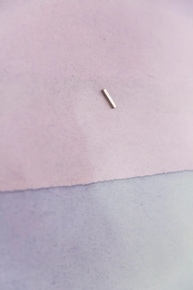 A small magnet sits on a piece of paper that is dyed half red and half blue as part of the litmus test.