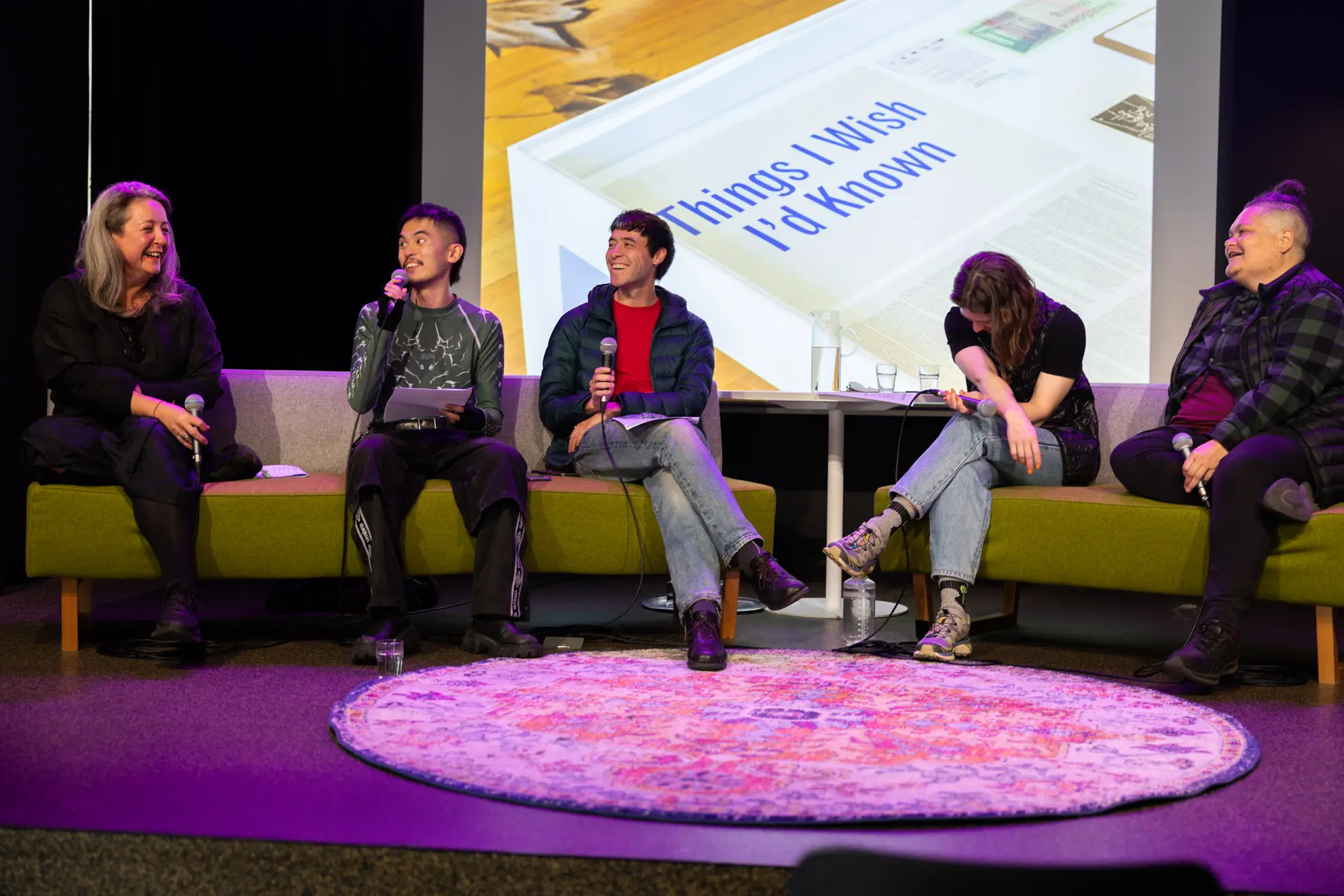 Panel discussion of 5 individuals. Frontal image of all of them. 4 out of 5 of them are looking at Lisa Radford, laughing. The other has their head tilted downward with their arms crossed.